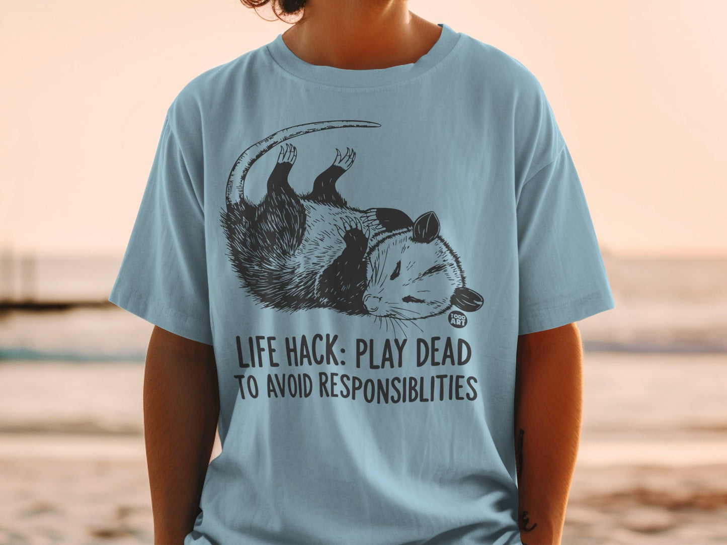 T-shirt with opossum graphic and "LIFE HACK: PLAY DEAD TO AVOID RESPONSIBILITIES" text.