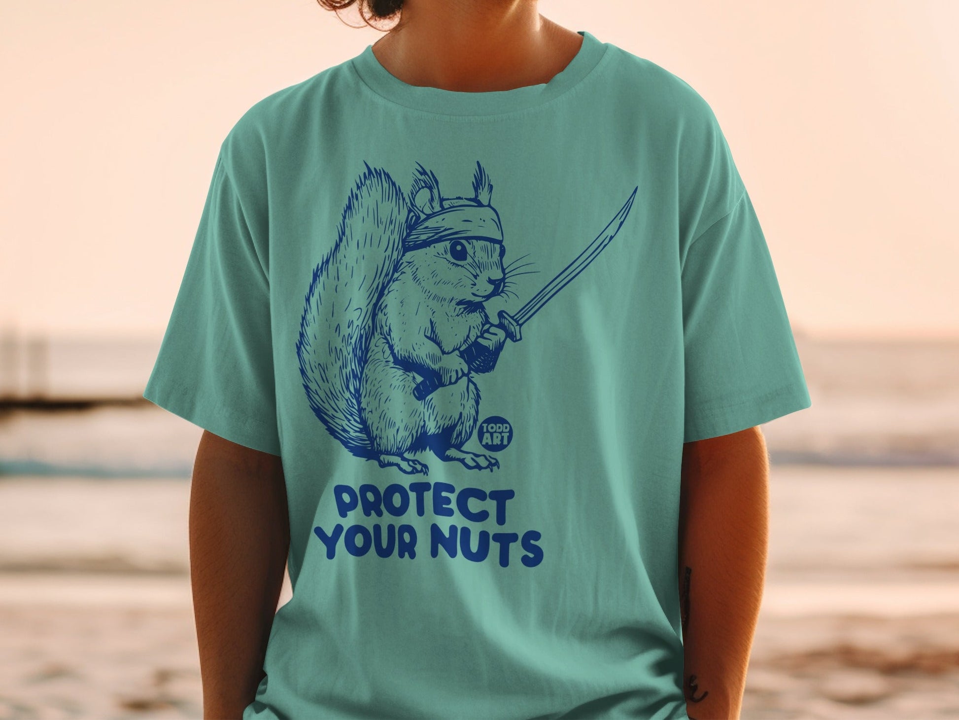 Teal t-shirt with a squirrel in a headband holding a katana and the text "PROTECT YOUR NUTS".