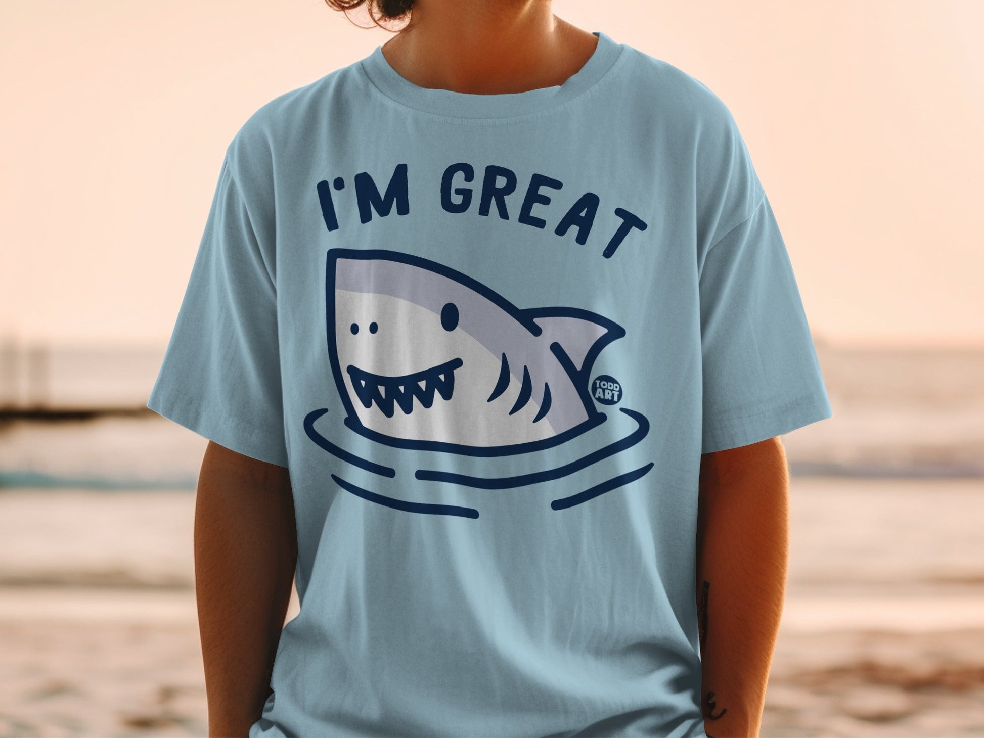Light blue t-shirt with a smiling shark design and text "I'M GREAT".