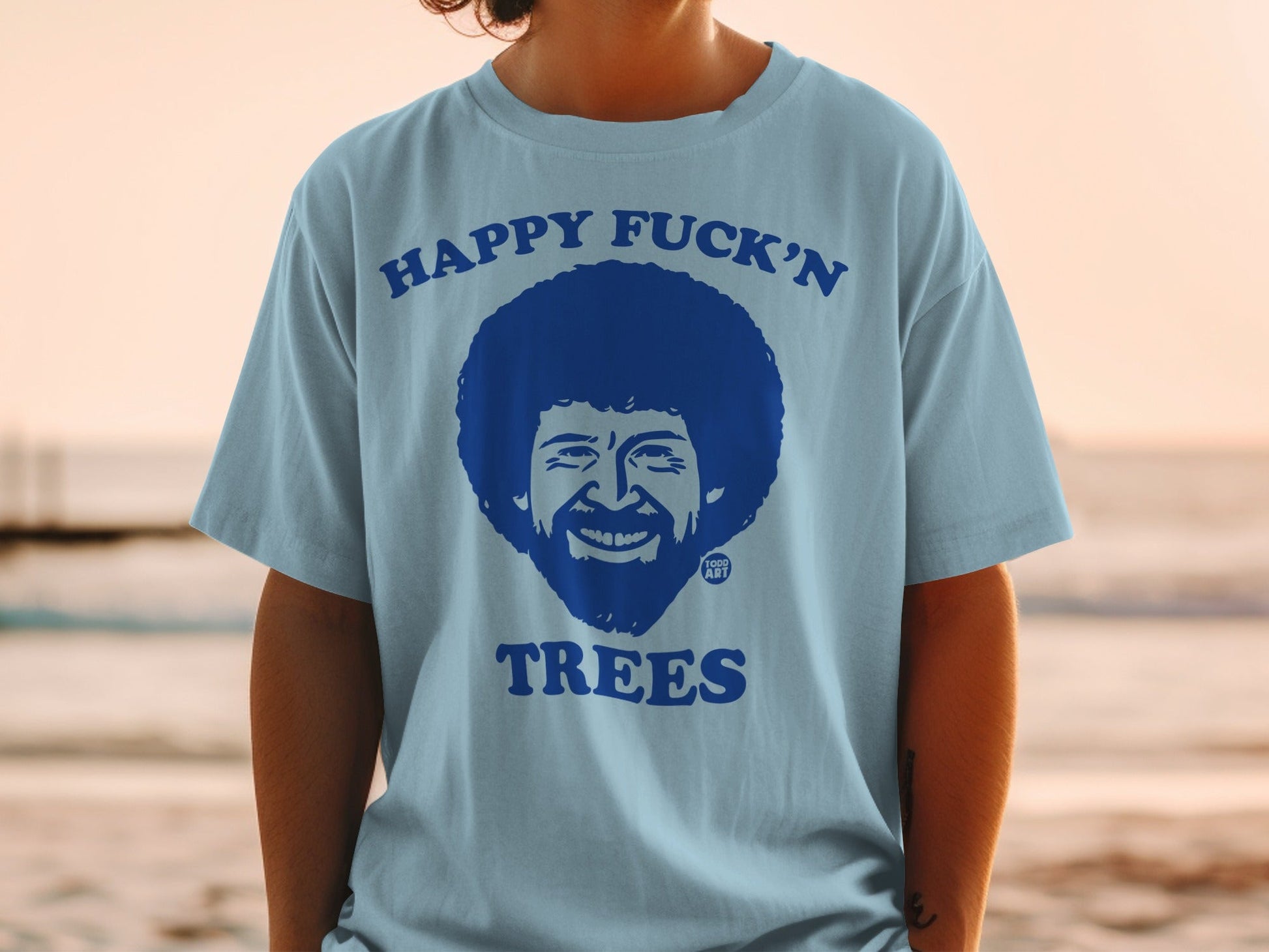 Light blue t-shirt with Bob Ross graphic and text "HAPPY FUCK'N TREES".