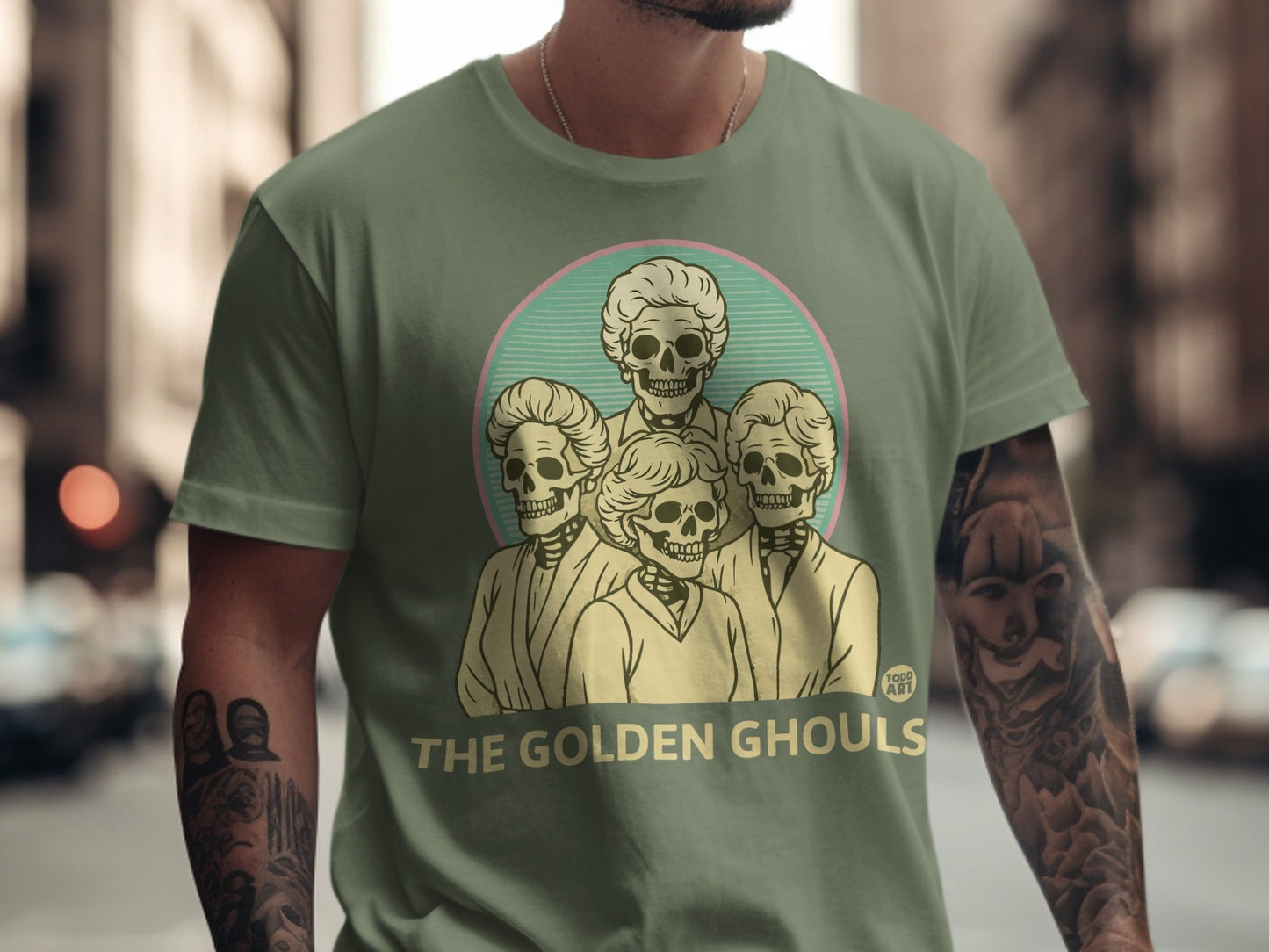 Graphic t-shirt featuring a pale green circle with four skeleton heads and text "THE GOLDEN GHOULS".