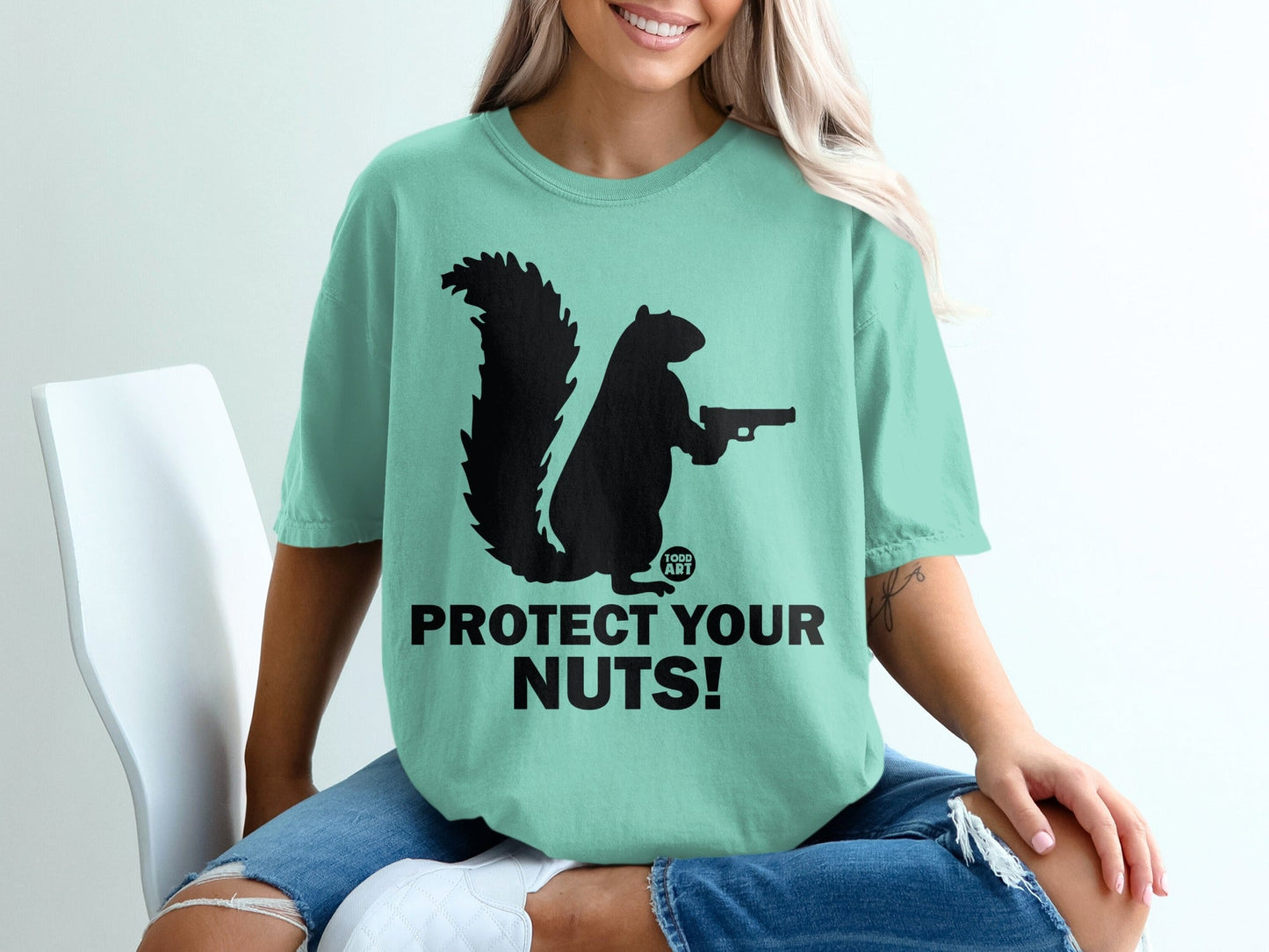 Black squirrel holding a gun with text "Protect Your Nuts!" on mint t-shirt.