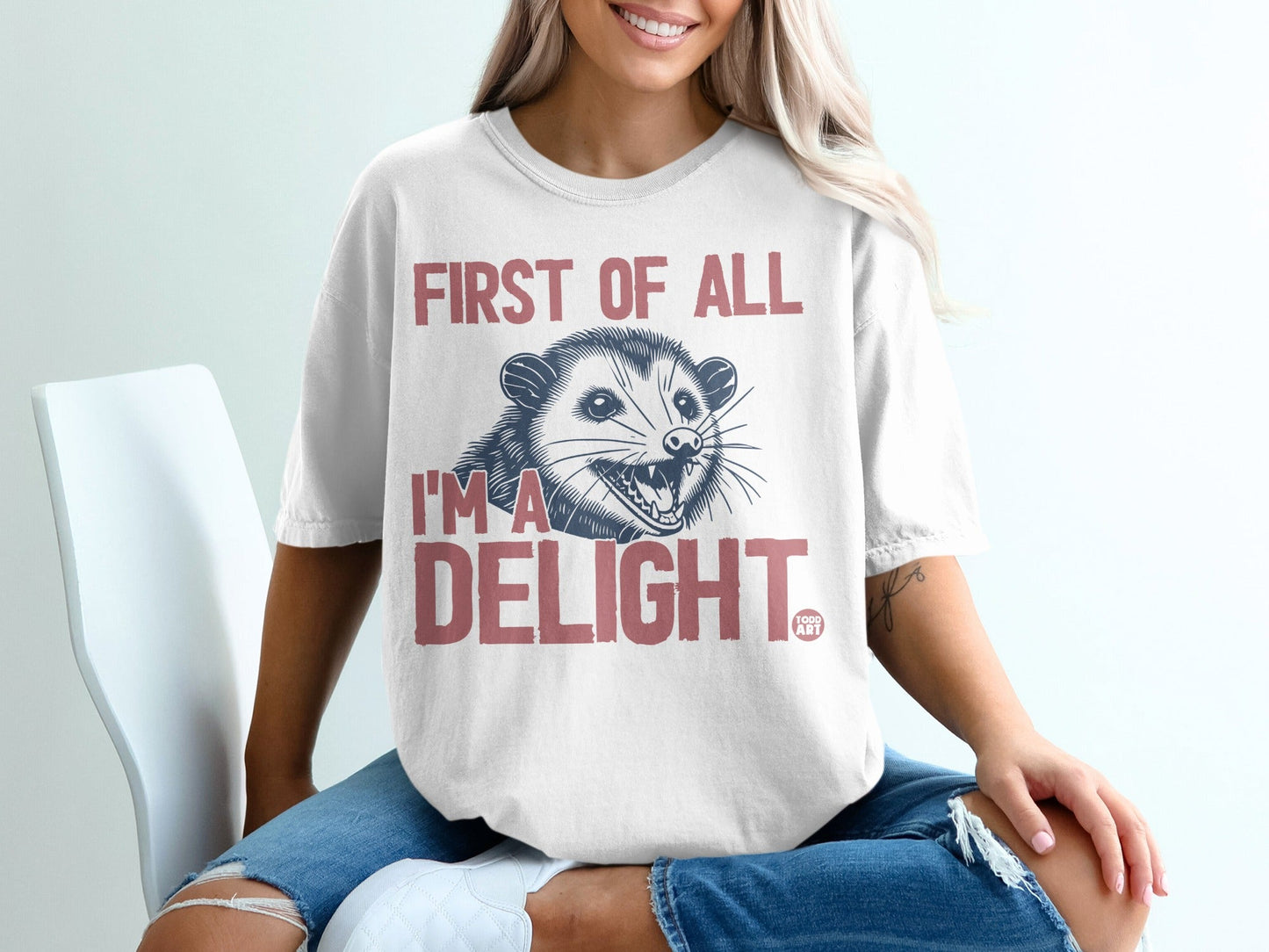White t-shirt with pink text "FIRST OF ALL I'M A DELIGHT" and a possum graphic.