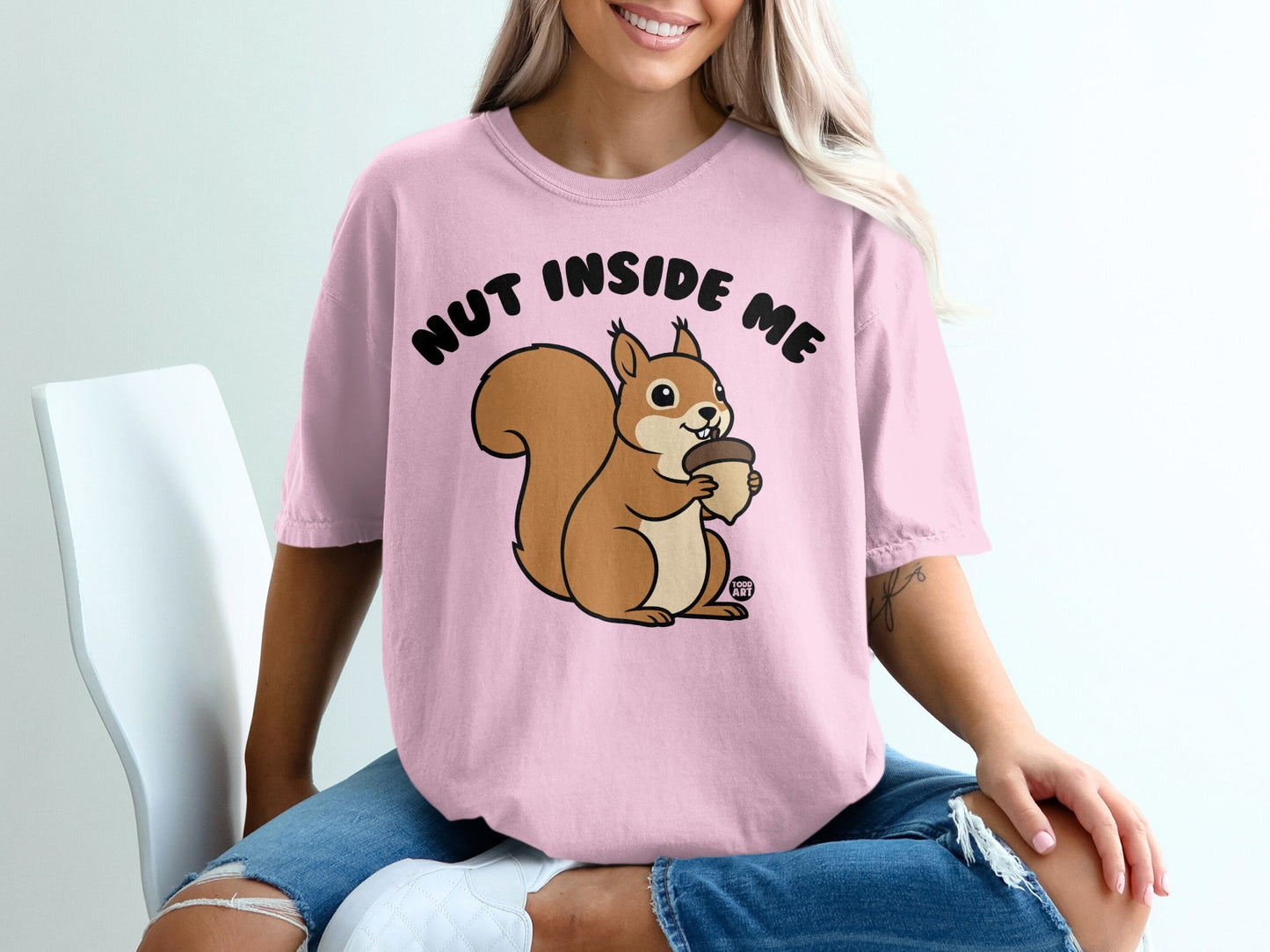 Pink t-shirt with cartoon squirrel holding acorn and text "NUT INSIDE ME".