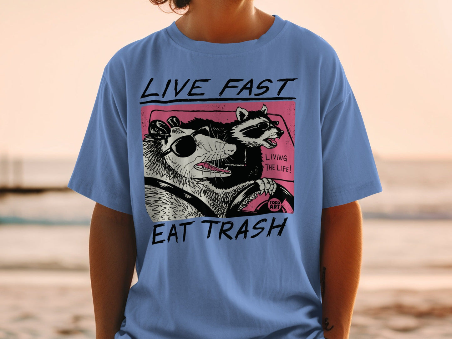 Blue t-shirt with raccoon and possum driving, "Live Fast Eat Trash" text.