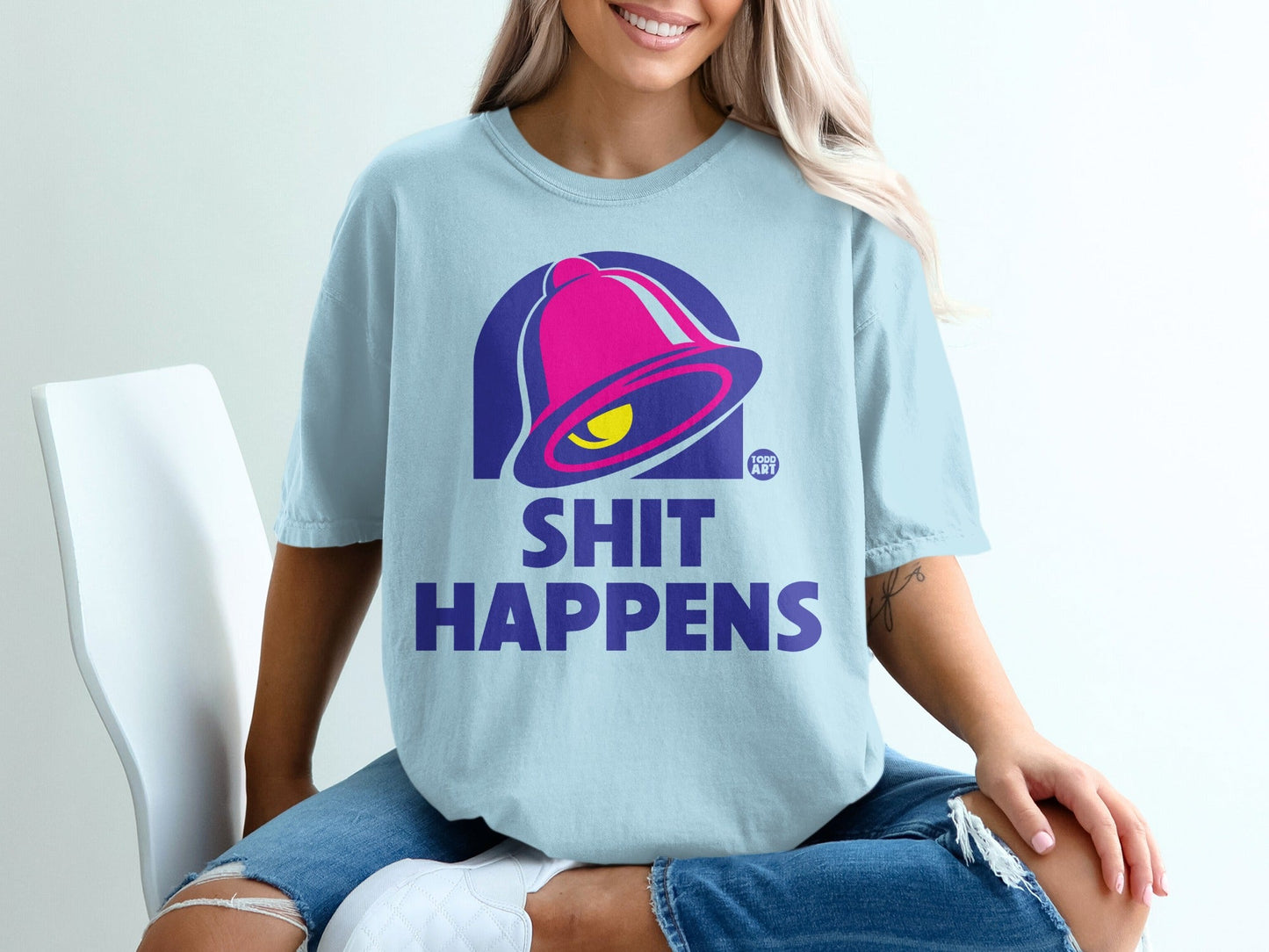 Light blue t-shirt with pink and yellow bell logo and "SHIT HAPPENS" text.