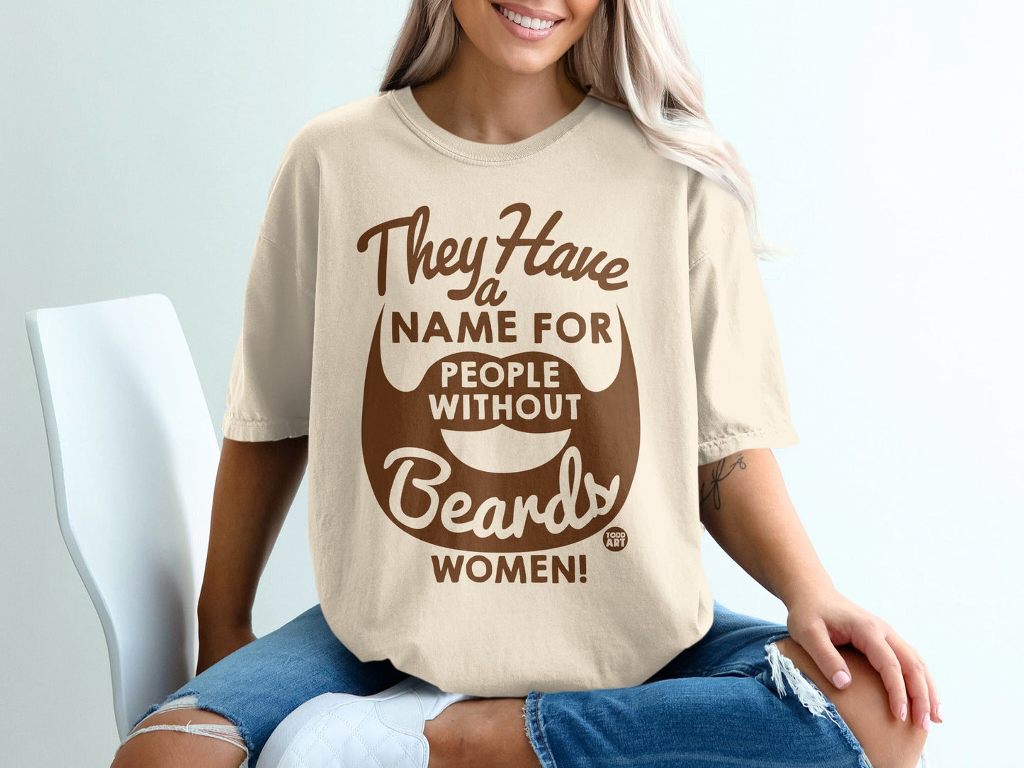 Light beige t-shirt with brown text and a beard graphic, "They Have A Name For People Without Beards WOMEN!".