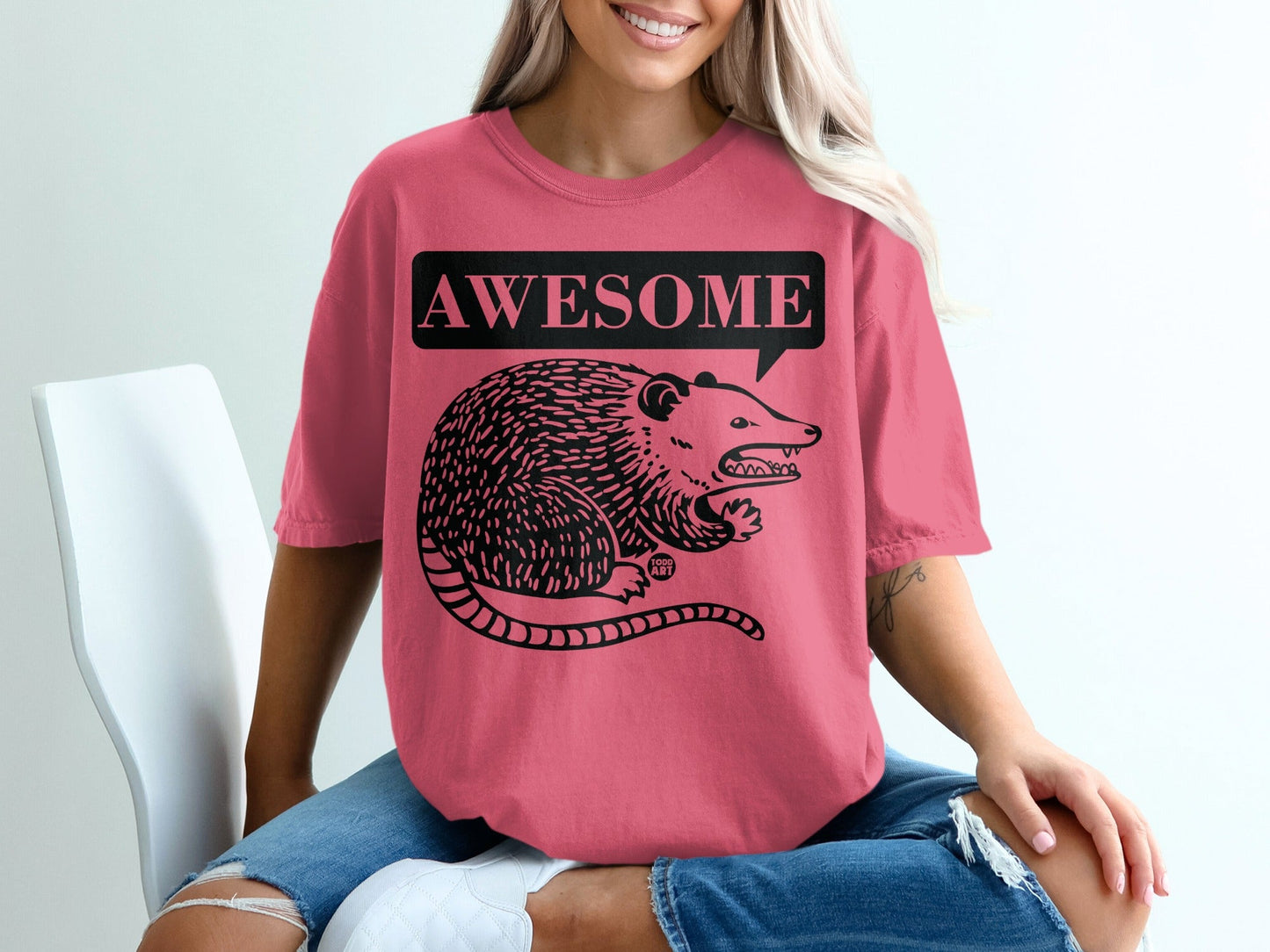 Pink t-shirt with a black graphic of a possum in a speech bubble that says "AWESOME".