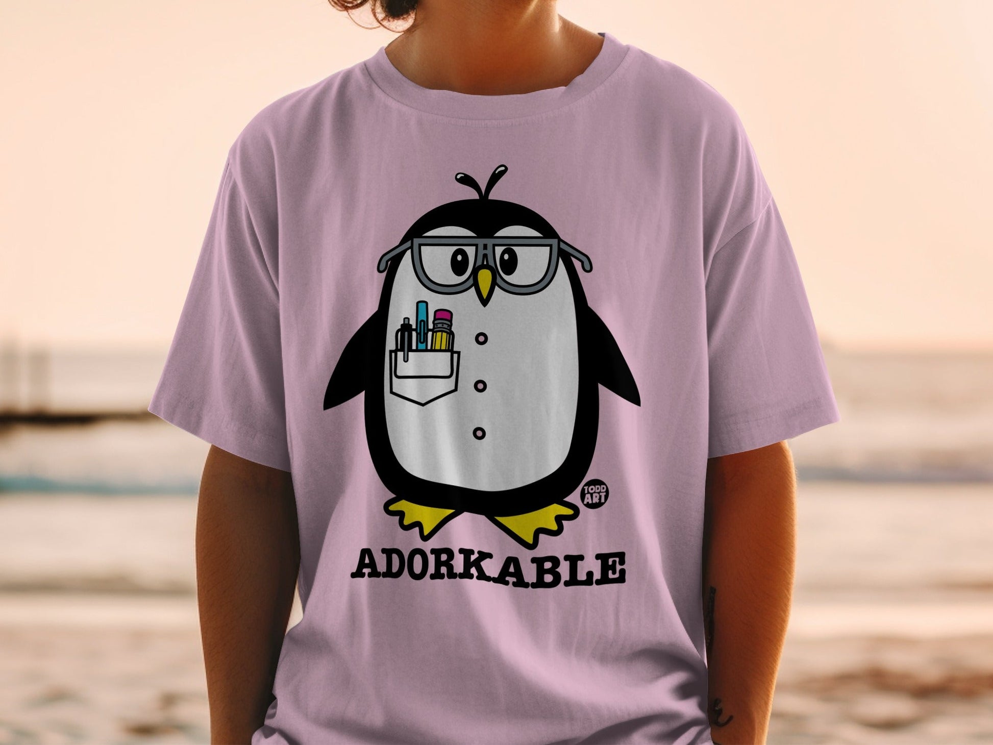 Pink t-shirt with cartoon penguin wearing glasses and holding pens.