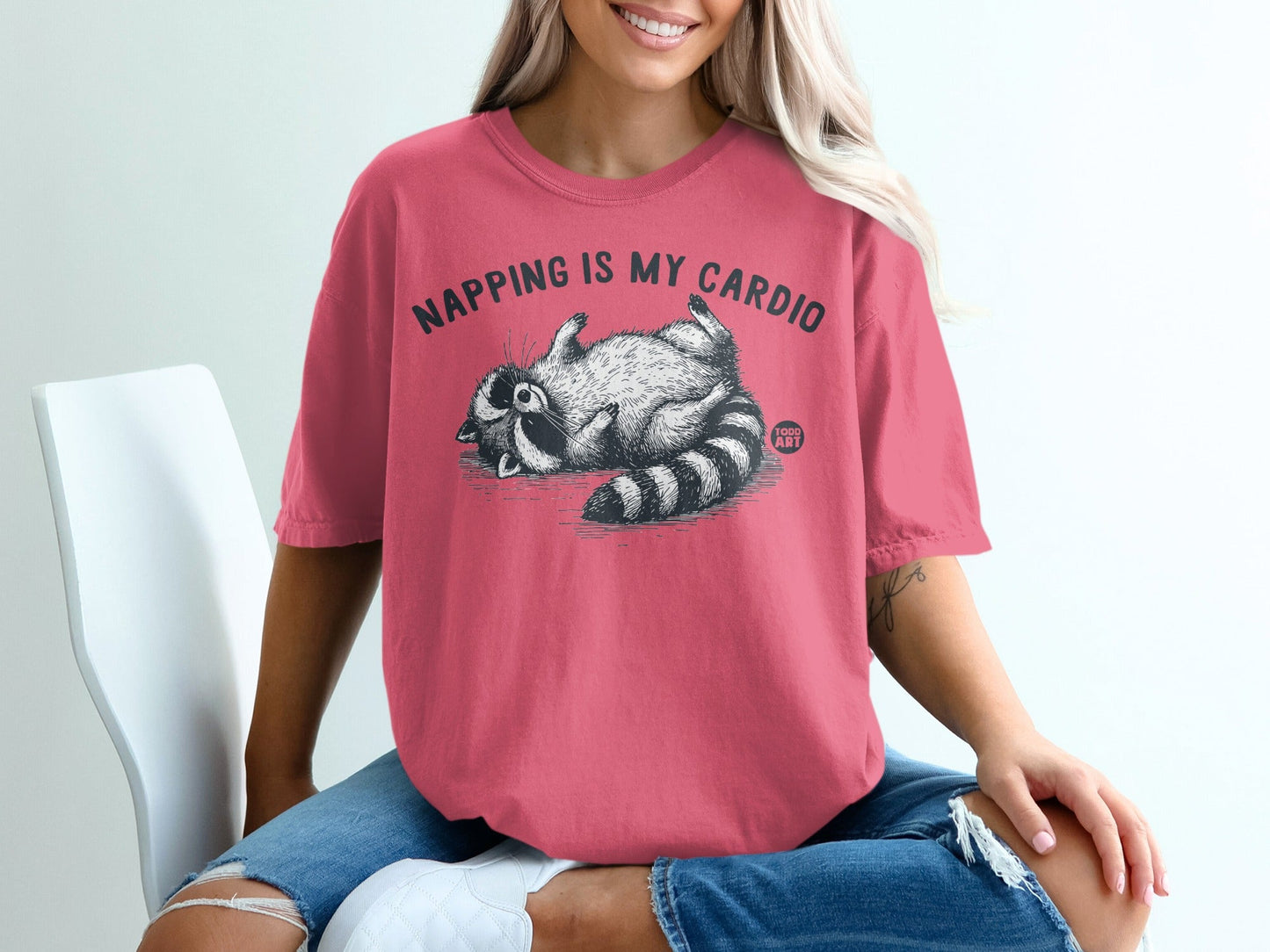 Pink t-shirt with raccoon graphic and text "Napping is my cardio".