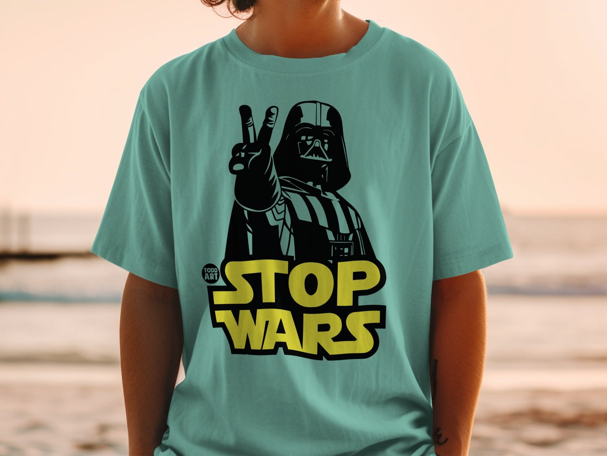 Darth Vader gives peace sign on teal t-shirt with "STOP WARS" text.