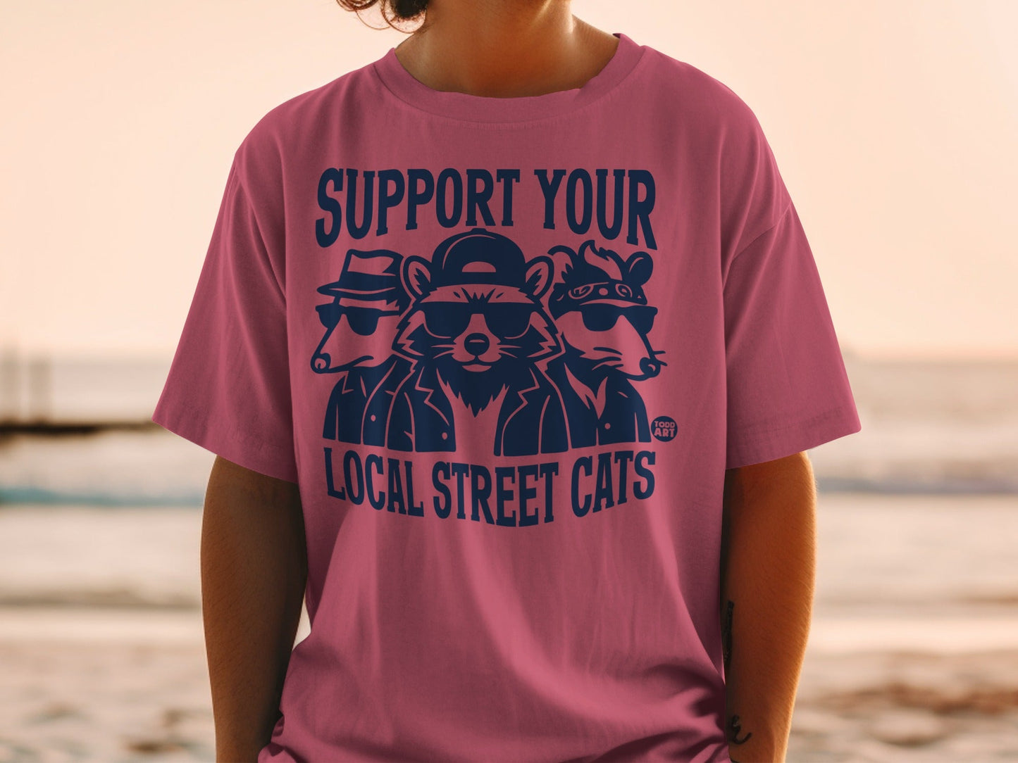 T-shirt with three raccoons wearing sunglasses and hats, text "SUPPORT YOUR LOCAL STREET CATS".