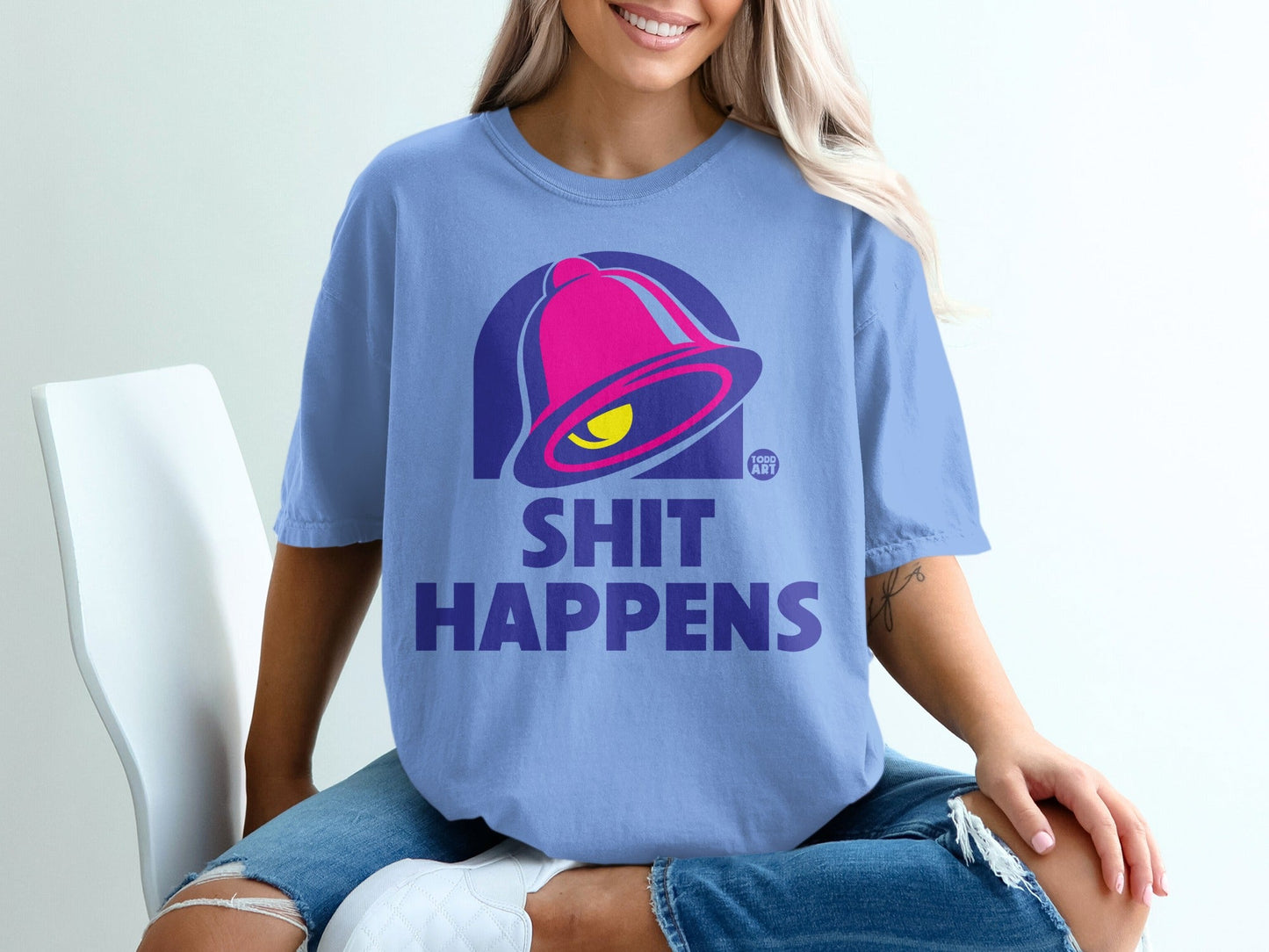 Purple t-shirt with a pink bell logo and "SHIT HAPPENS" text.
