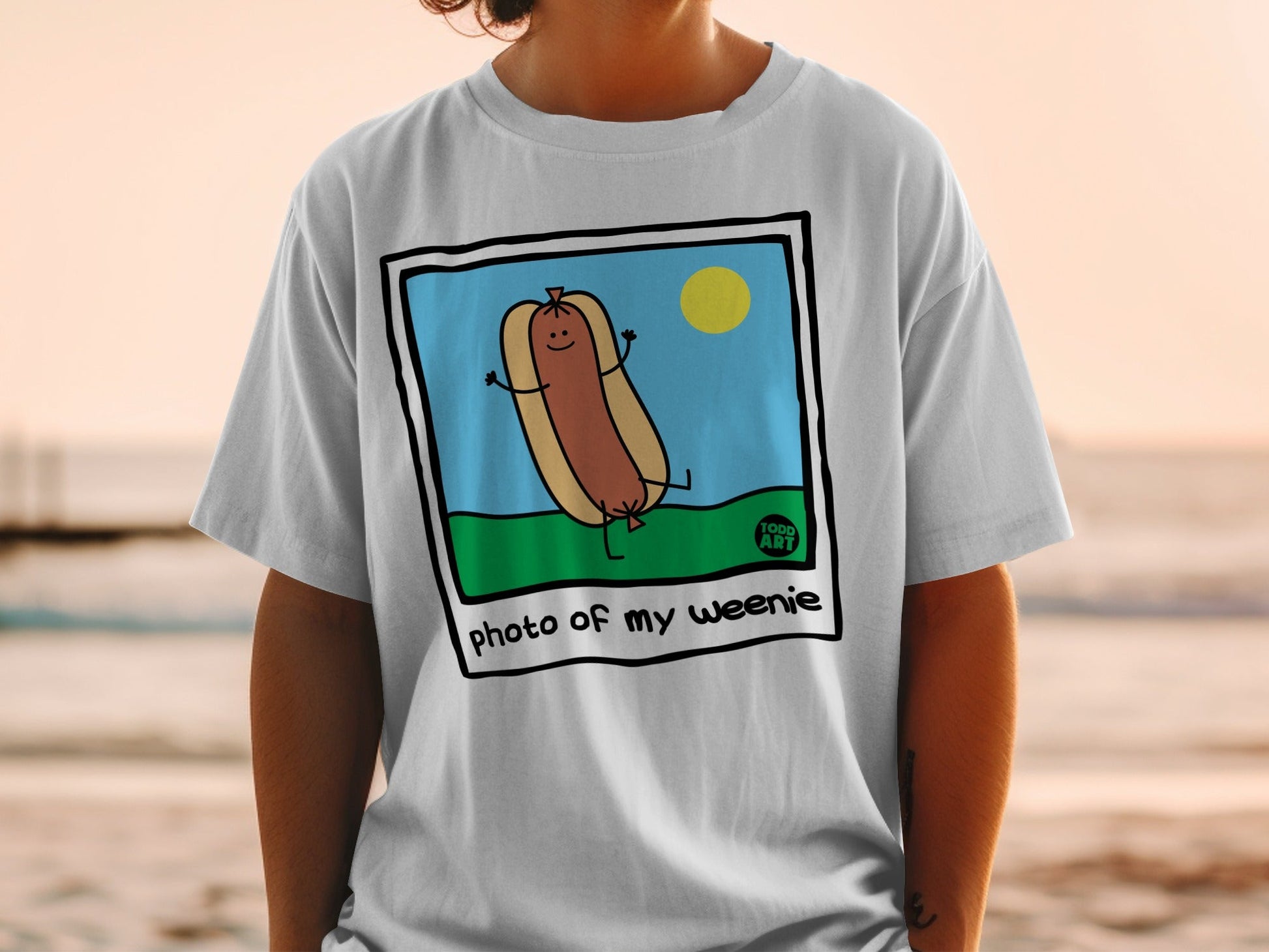 Cartoon hot dog with arms raised, on a t-shirt with "photo of my weenie" text.