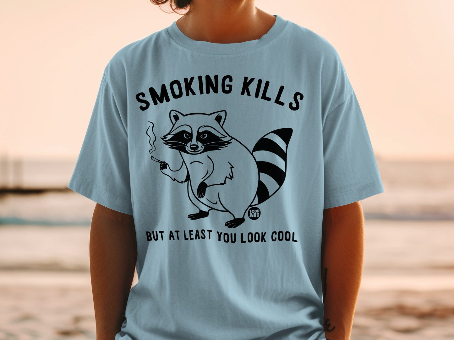 Light blue t-shirt with raccoon smoking and text "Smoking kills but at least you look cool".