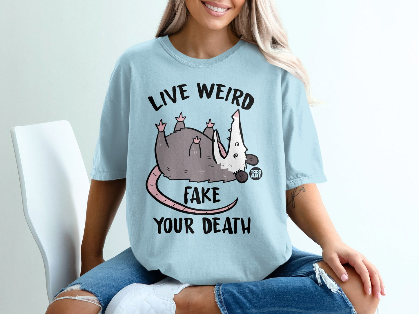 Light blue t-shirt with opossum graphic and text "Live Weird Fake Your Death".