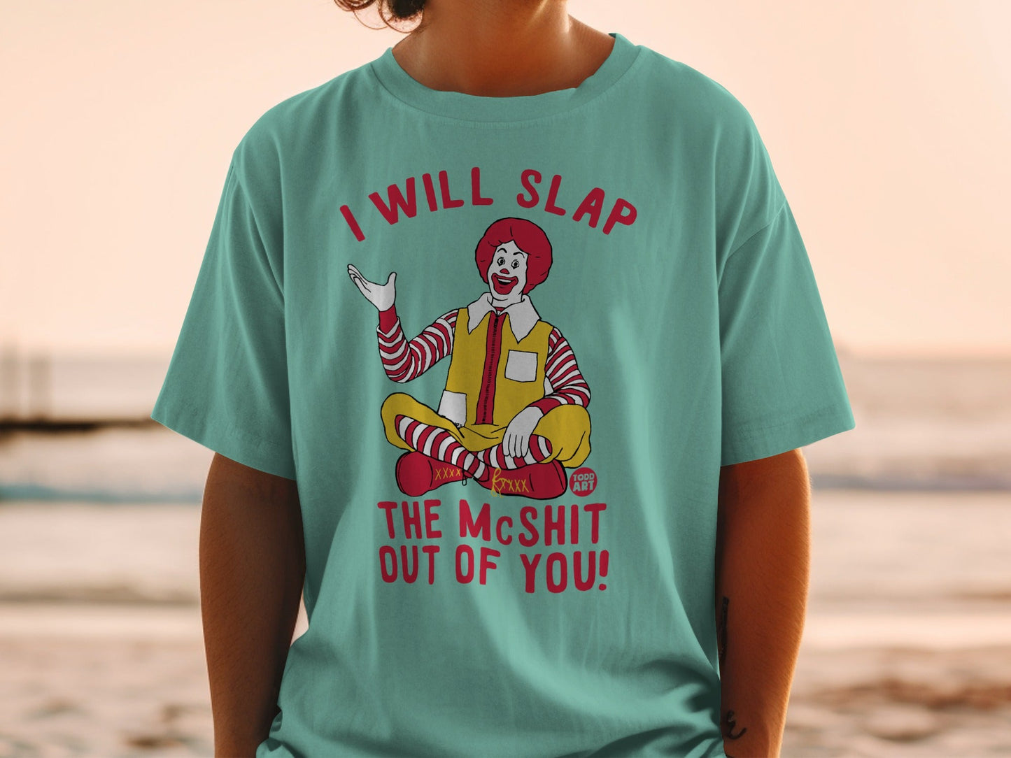 Ronald McDonald sitting cross-legged, wearing a teal t-shirt with text.