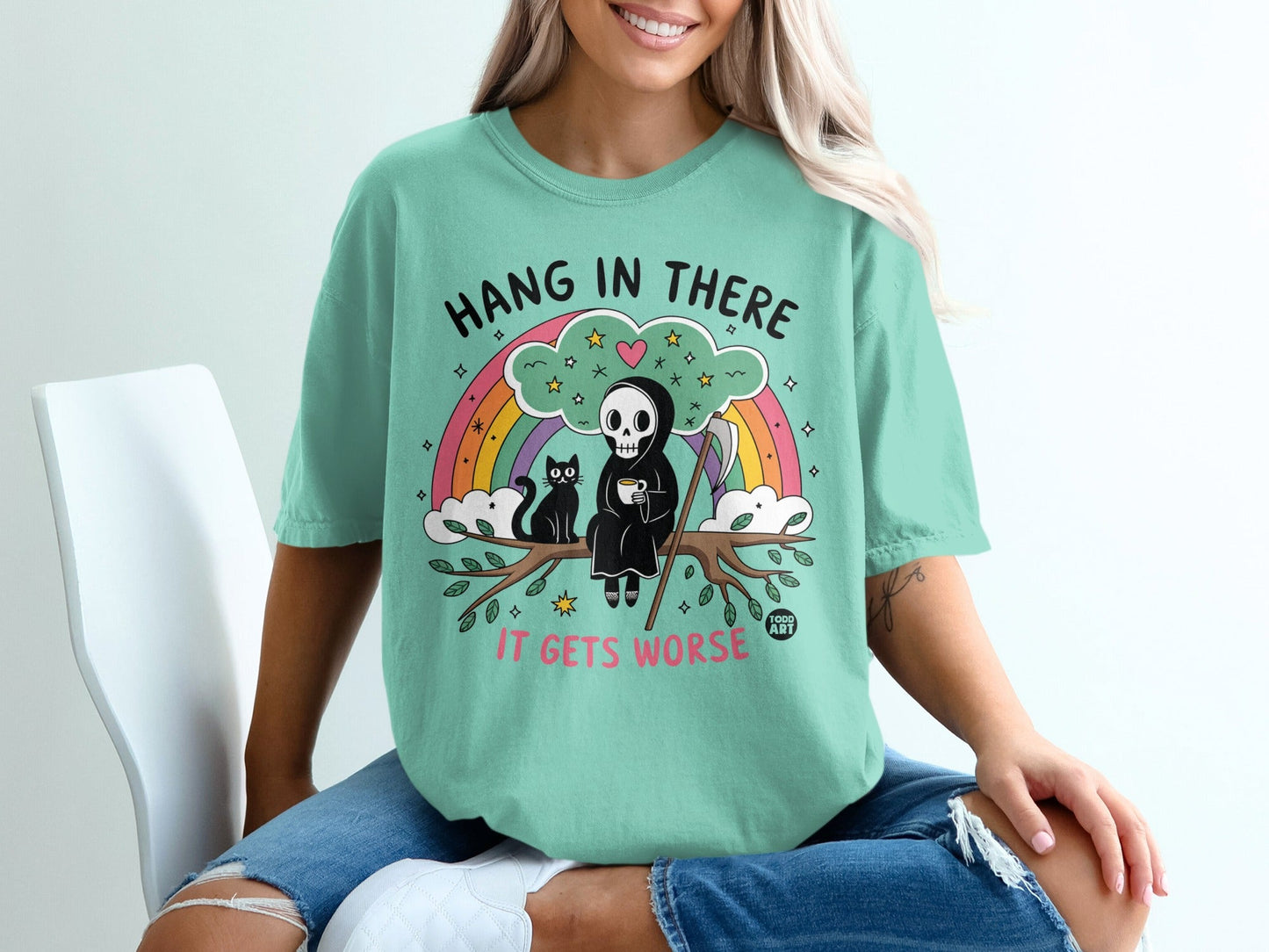 Mint green t-shirt with grim reaper holding coffee, sitting on a branch with text "HANG IN THERE IT GETS WORSE".