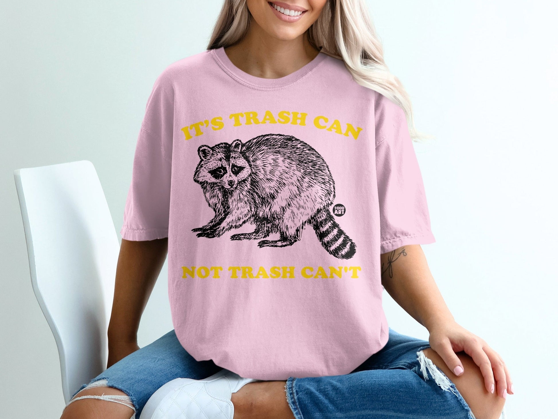 Pink t-shirt with raccoon graphic and text "IT'S TRASH CAN NOT TRASH CAN'T".