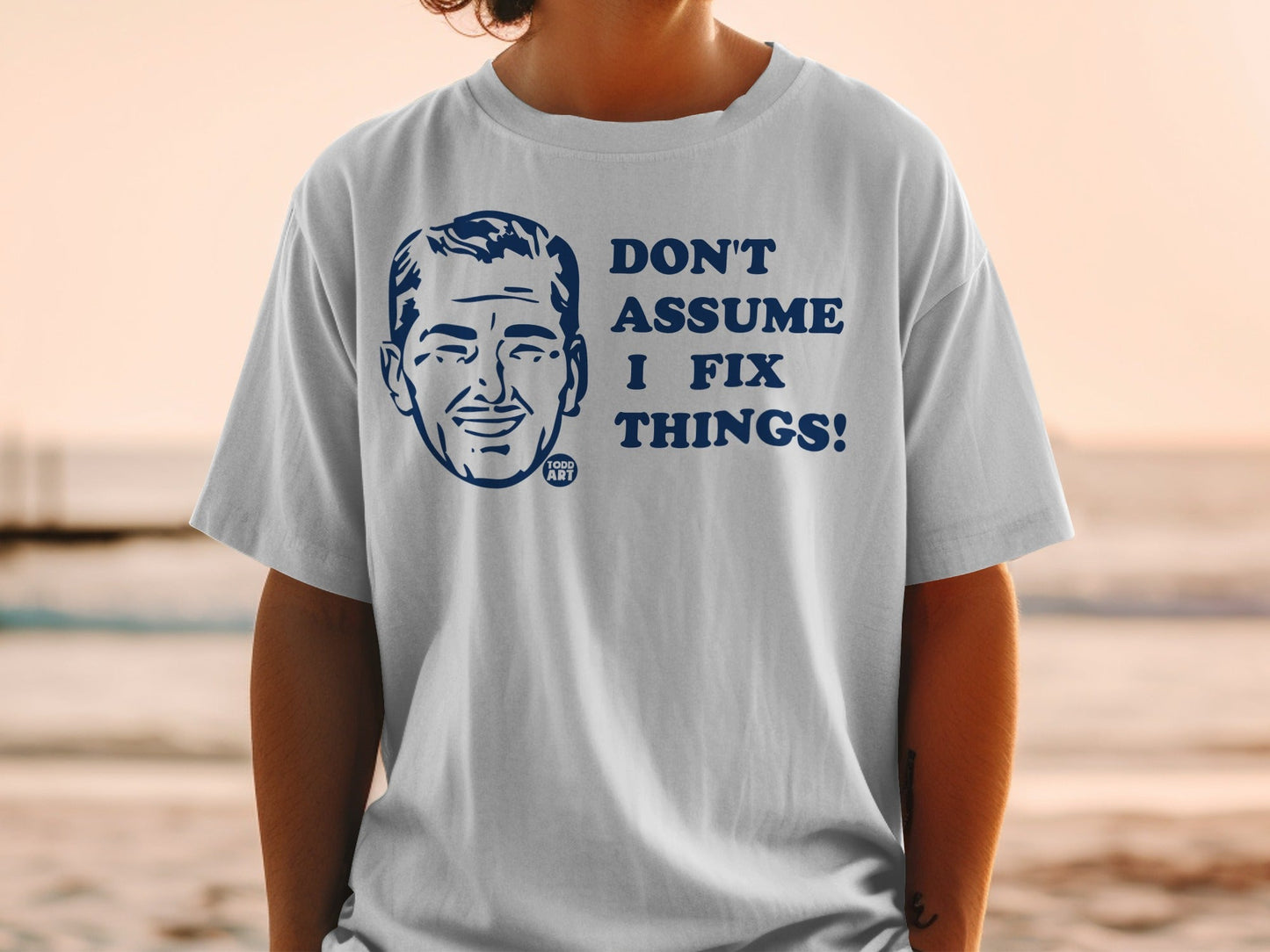 White t-shirt with a cartoon man's head and "DON'T ASSUME I FIX THINGS!"