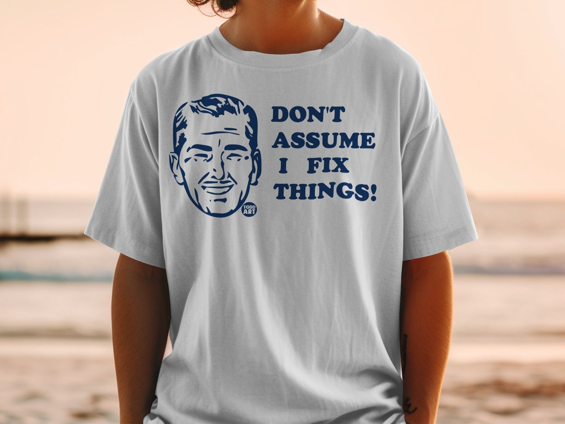 White t-shirt with a cartoon man's head and "DON'T ASSUME I FIX THINGS!"