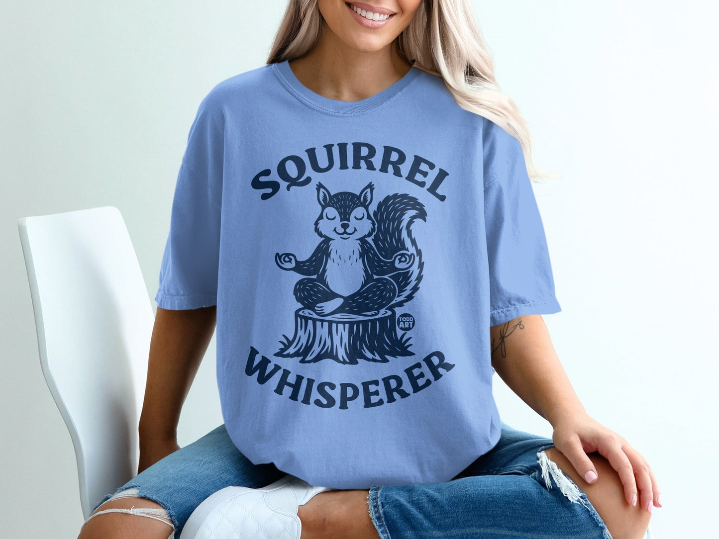 Blue t-shirt with a meditating squirrel on a tree stump, reading "Squirrel Whisperer."