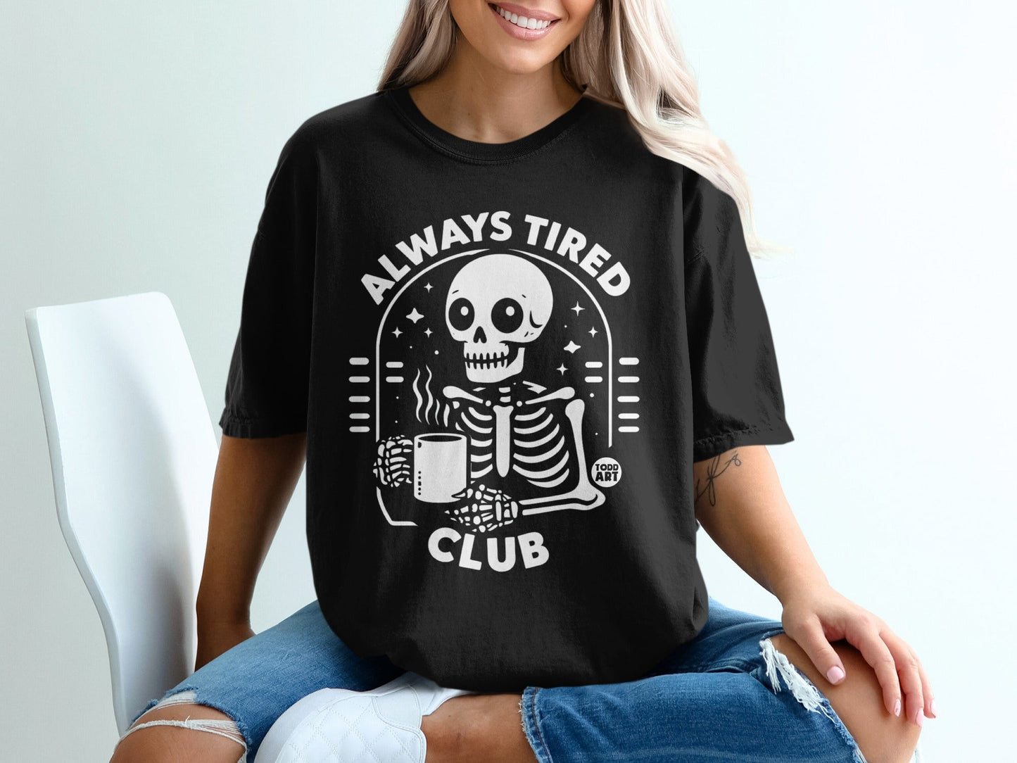 Black t-shirt with skeleton holding coffee cup and text "Always Tired Club".