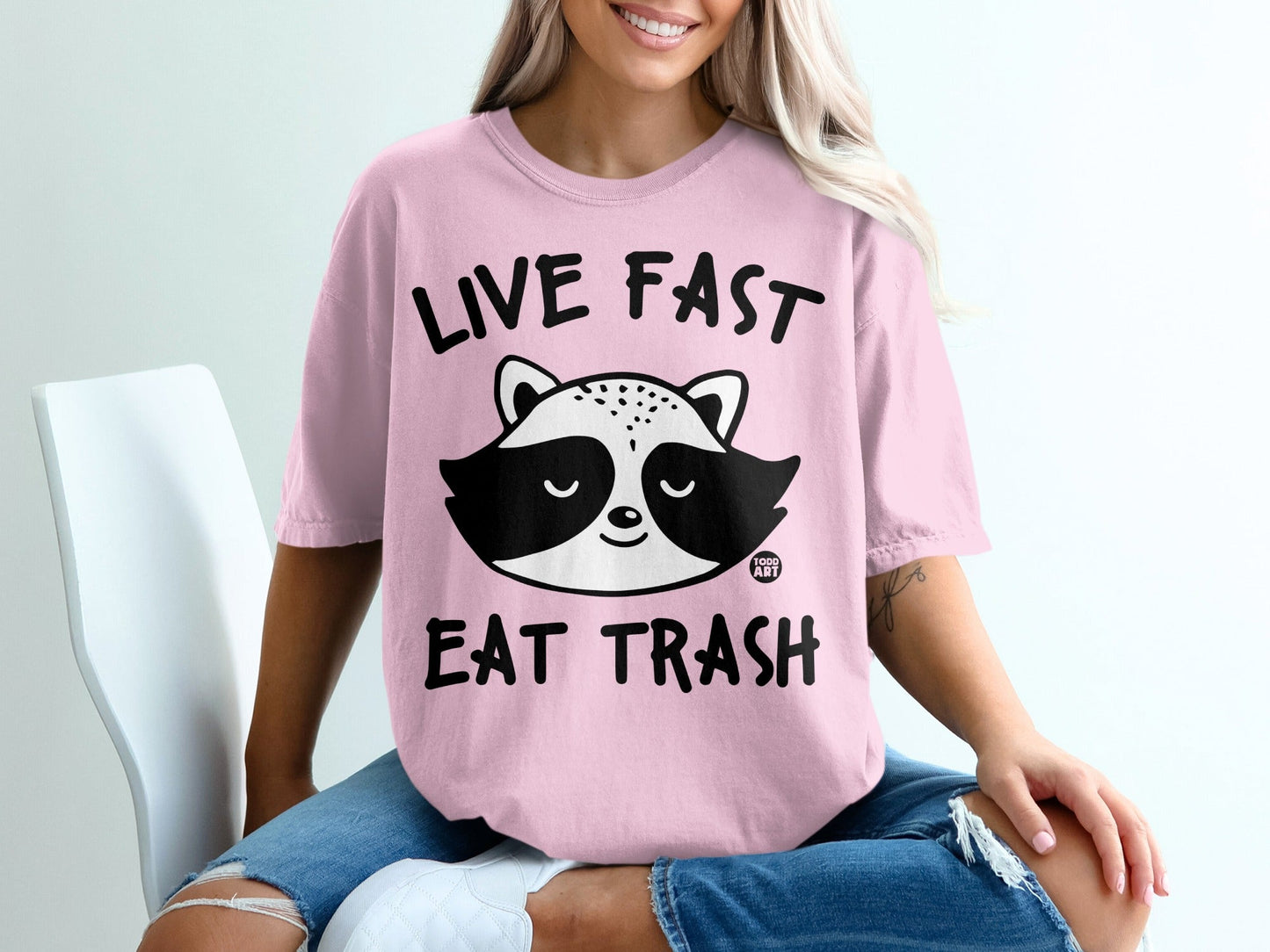 Pink t-shirt with raccoon graphic and text "LIVE FAST EAT TRASH."