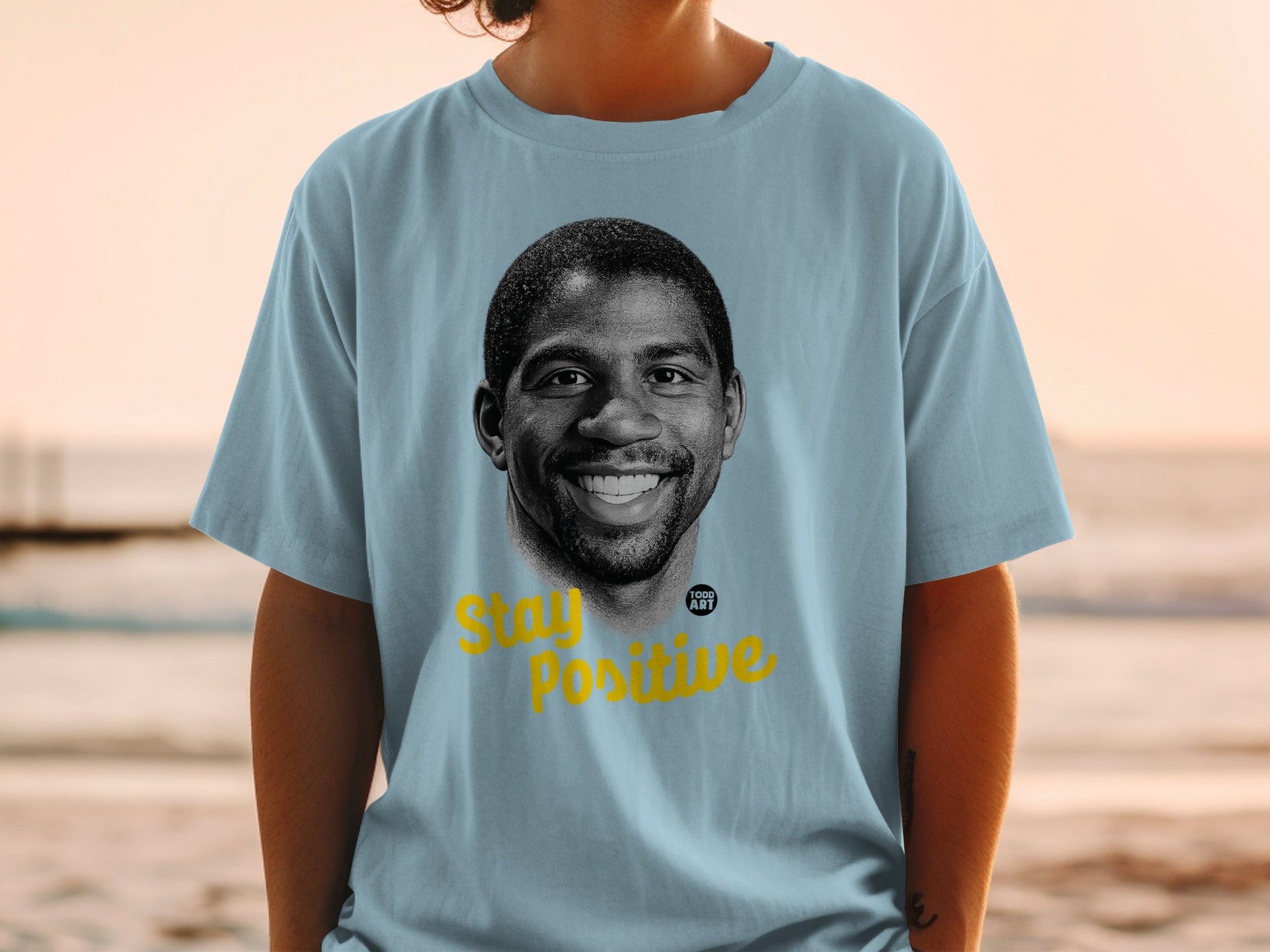Light blue t-shirt with portrait of Magic Johnson and "Stay Positive" text.