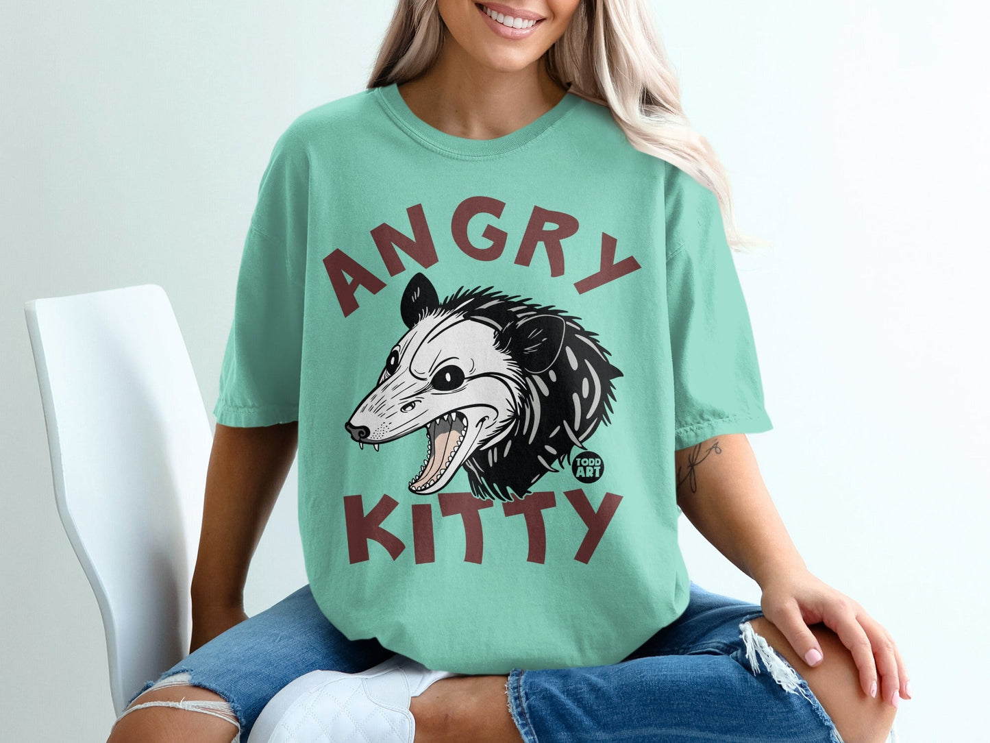 T-shirt with a teal graphic featuring an angry opossum and "ANGRY KITTY" text.