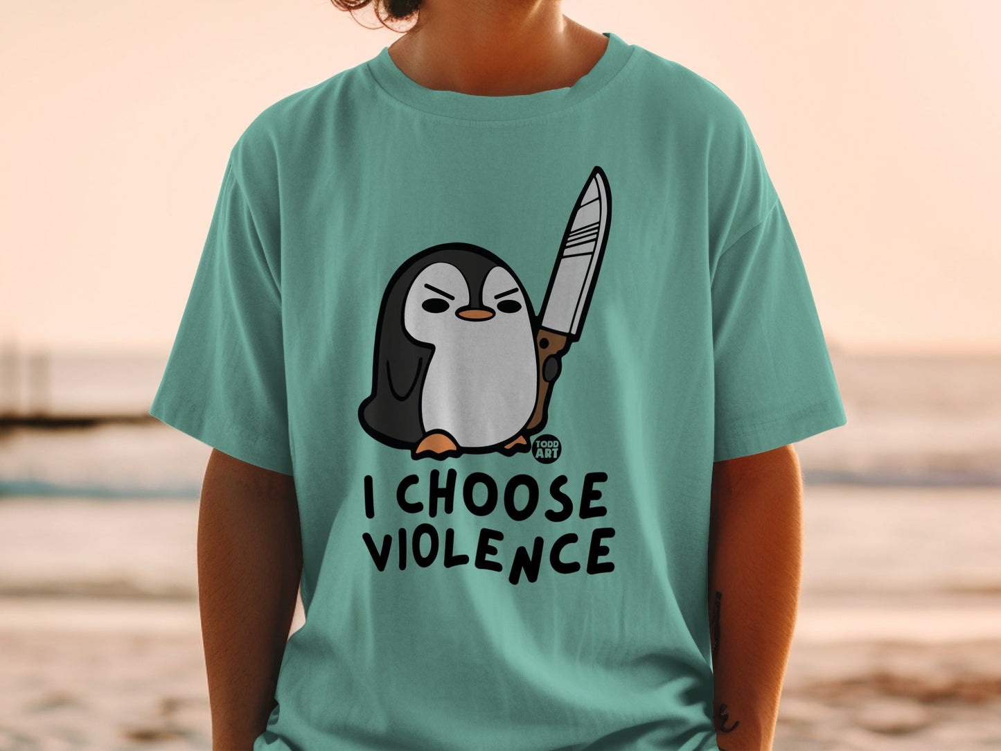 Penguin with knife and text "I CHOOSE VIOLENCE" on a teal t-shirt.