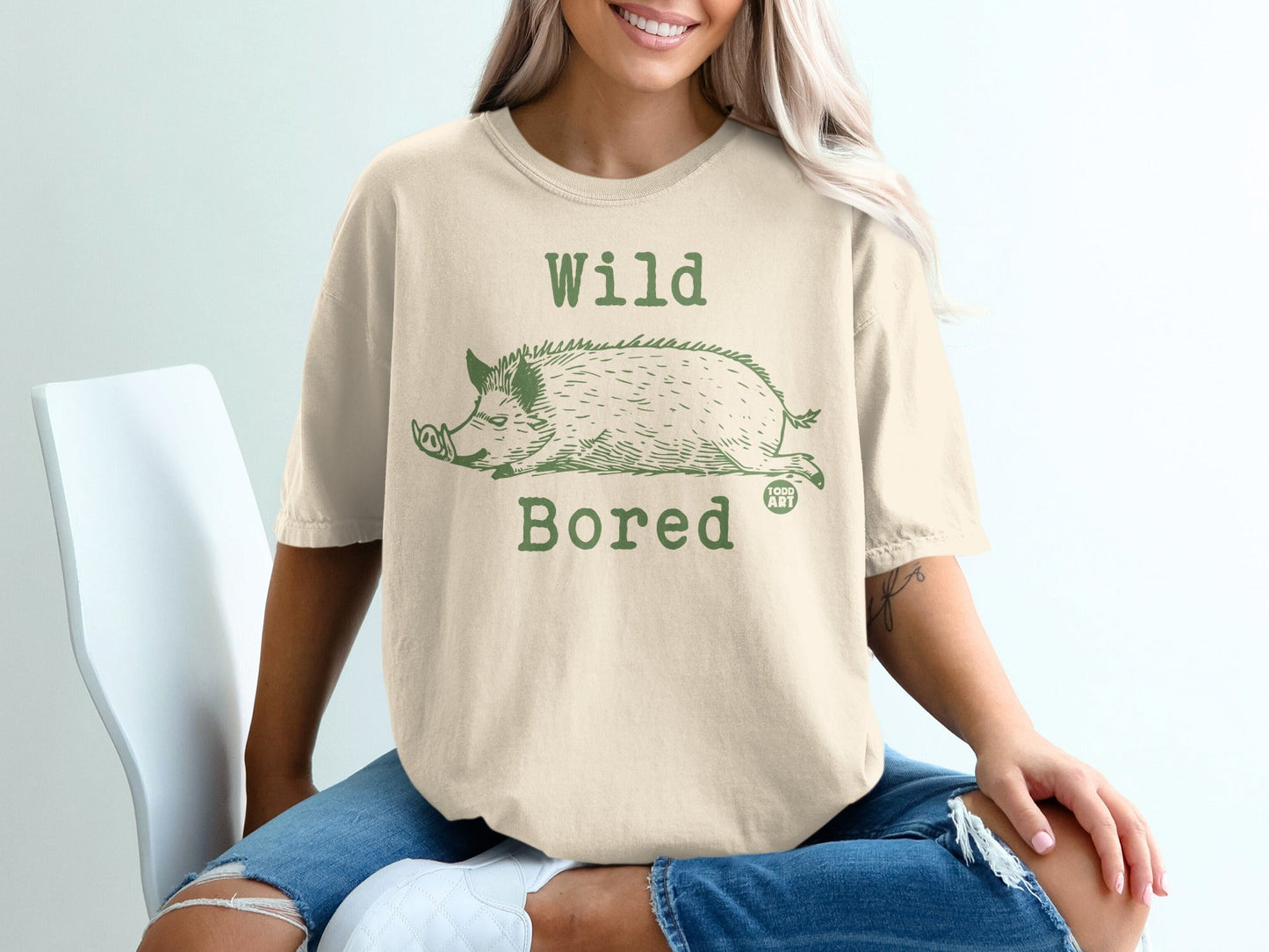 Cream t-shirt with green "Wild Bored" text and a sleeping wild boar graphic.