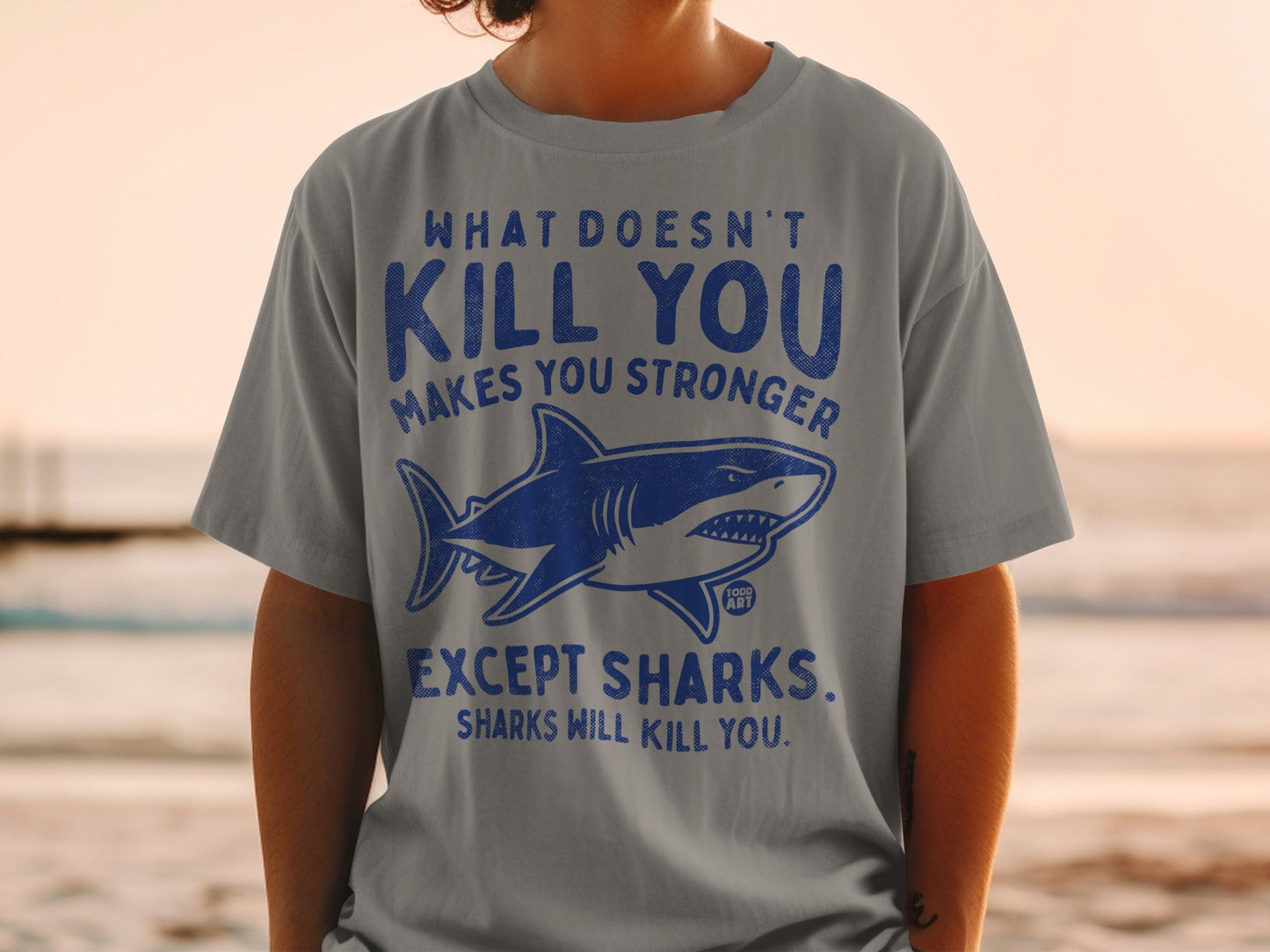 Gray t-shirt with shark graphic and text "What doesn't kill you makes you stronger except sharks."
