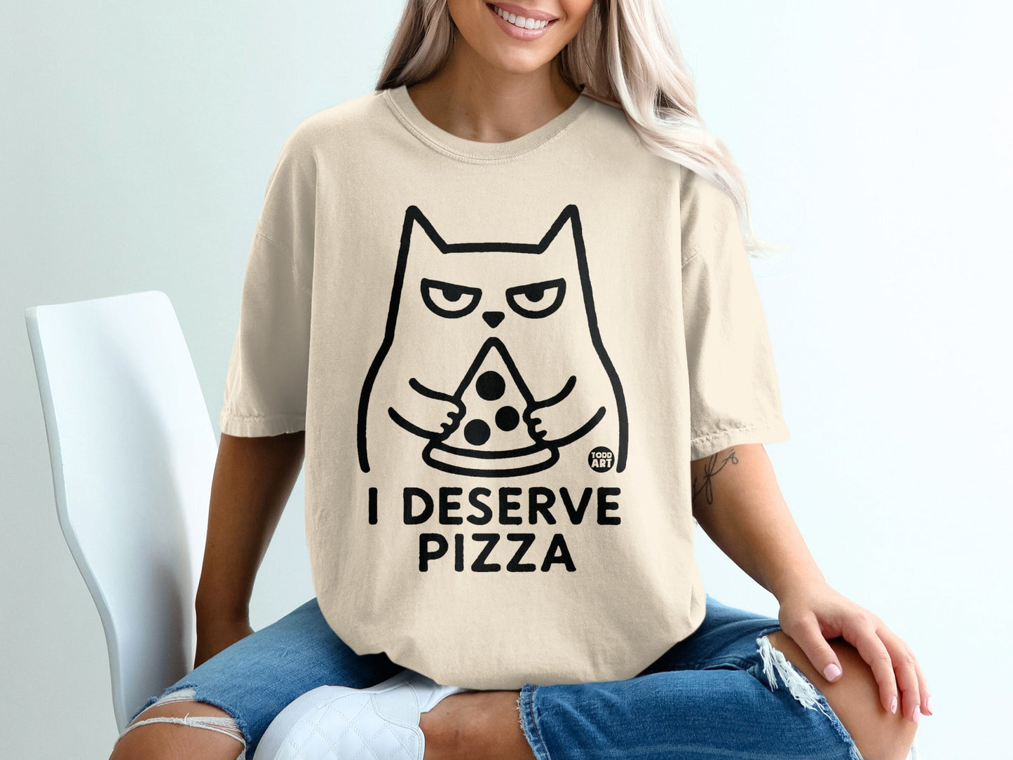 Cream t-shirt with black line drawing of a cat holding pizza, text "I DESERVE PIZZA".