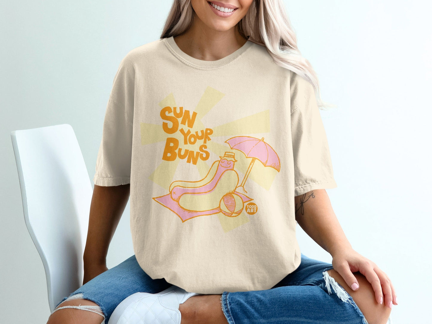T-shirt graphic of a hot dog on a beach chair under an umbrella.