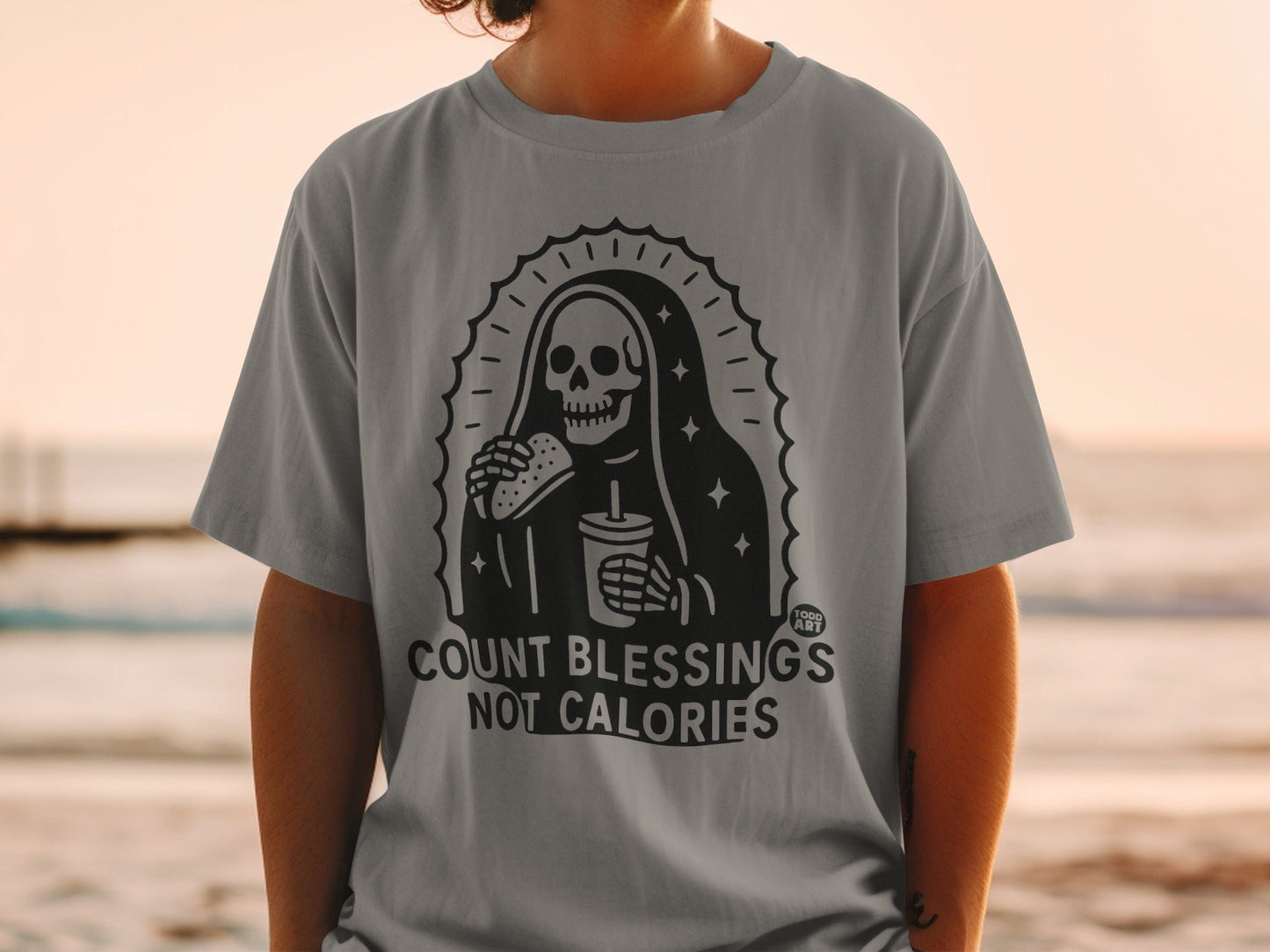 Gray t-shirt with skeleton Grim Reaper holding burger and drink, text "COUNT BLESSINGS NOT CALORIES".
