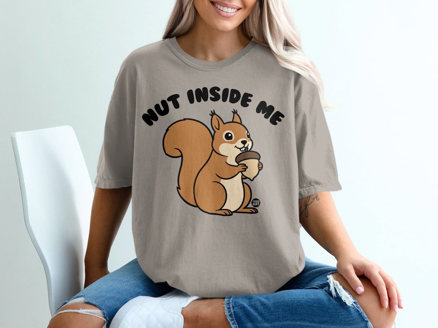Squirrel holding acorn with "Nut Inside Me" text on a beige t-shirt.