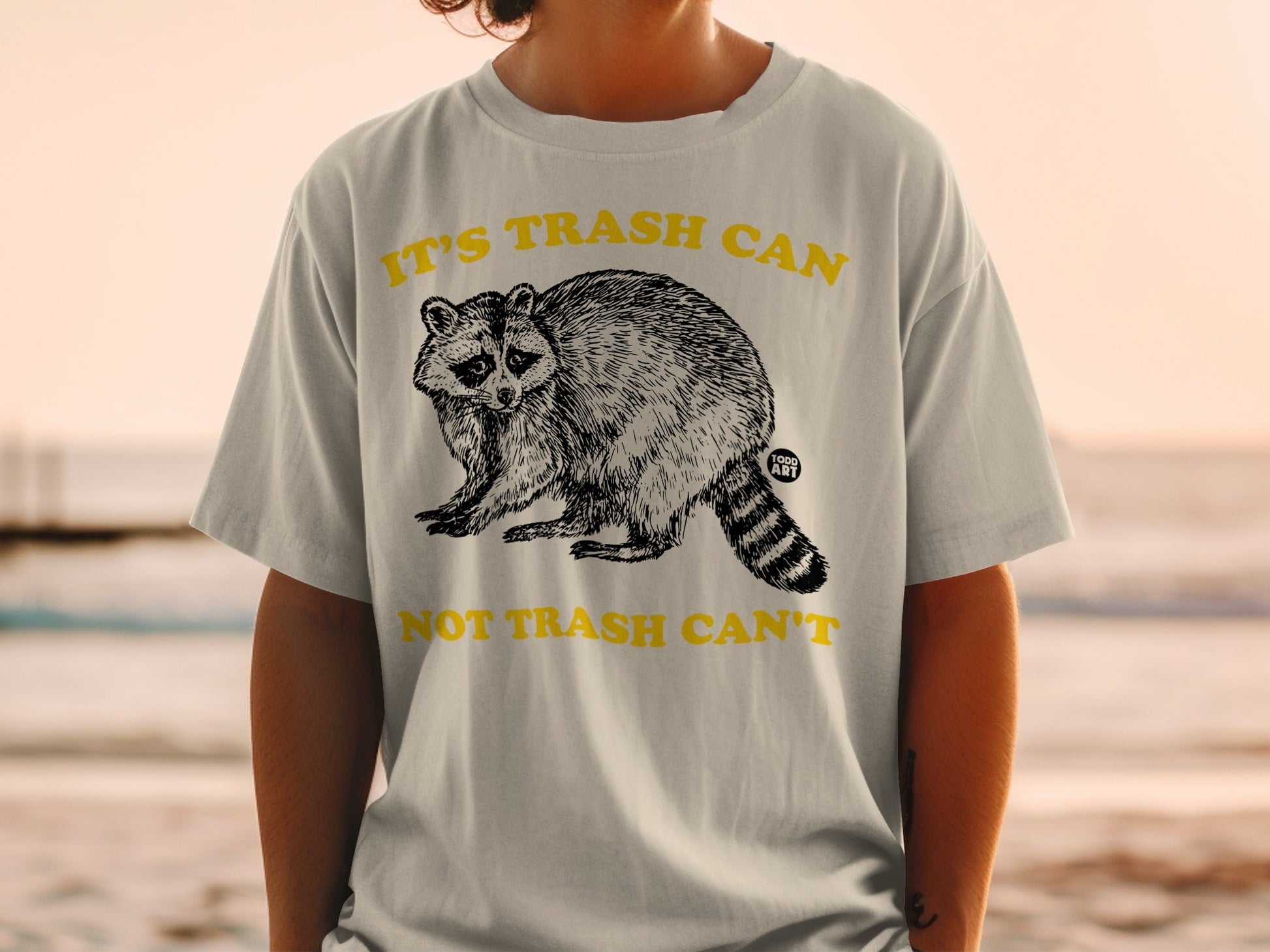 T-shirt with raccoon graphic and text "IT'S TRASH CAN NOT TRASH CAN'T"