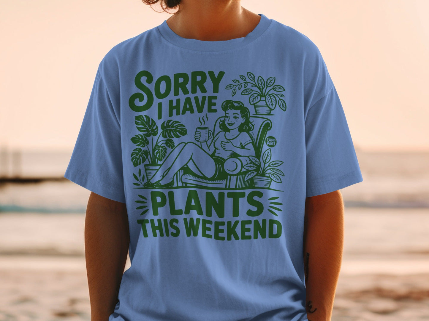 Blue t-shirt with green text and illustrations of plants and a woman drinking coffee.