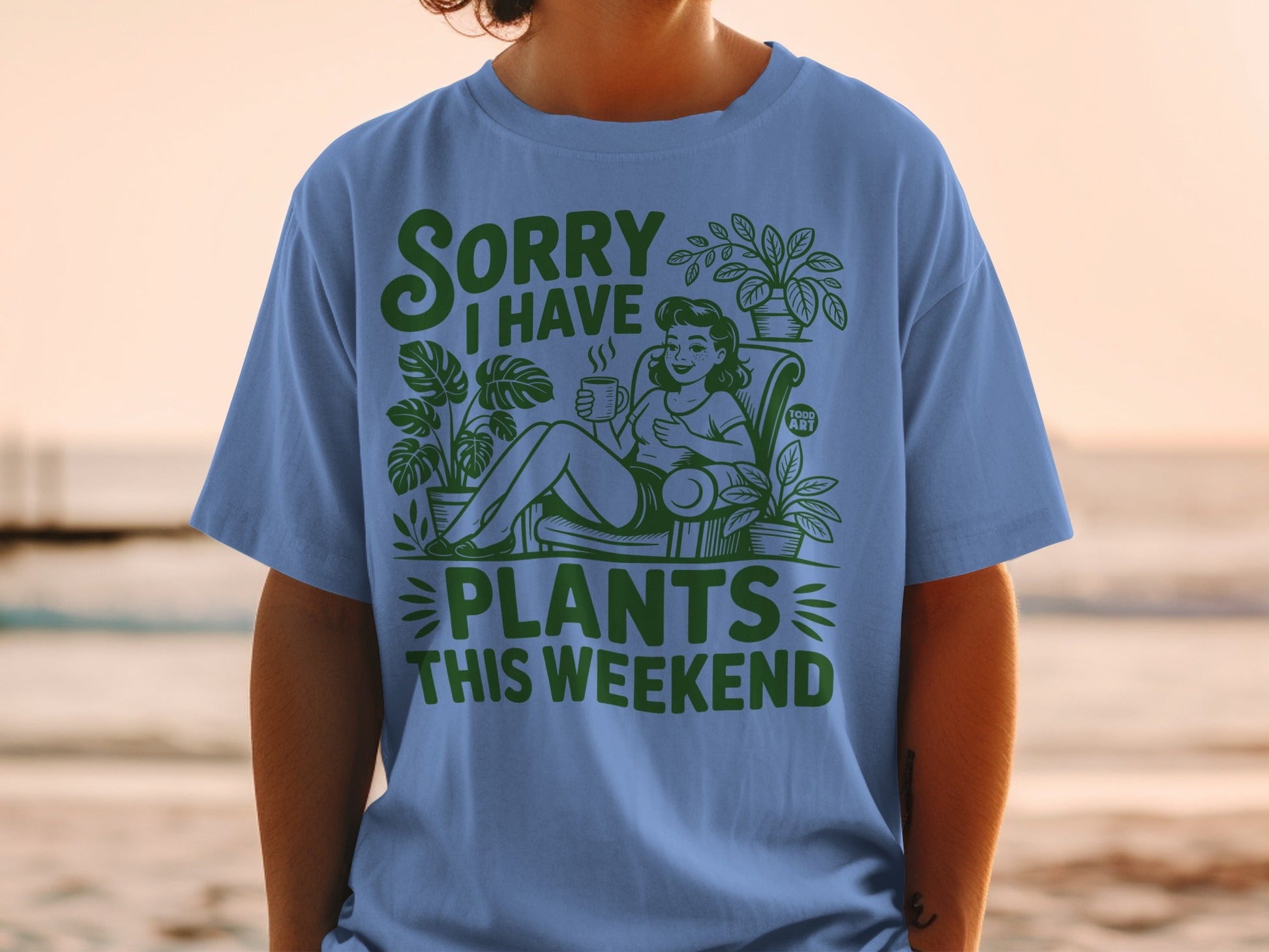 Blue t-shirt with green text and illustrations of plants and a woman drinking coffee.