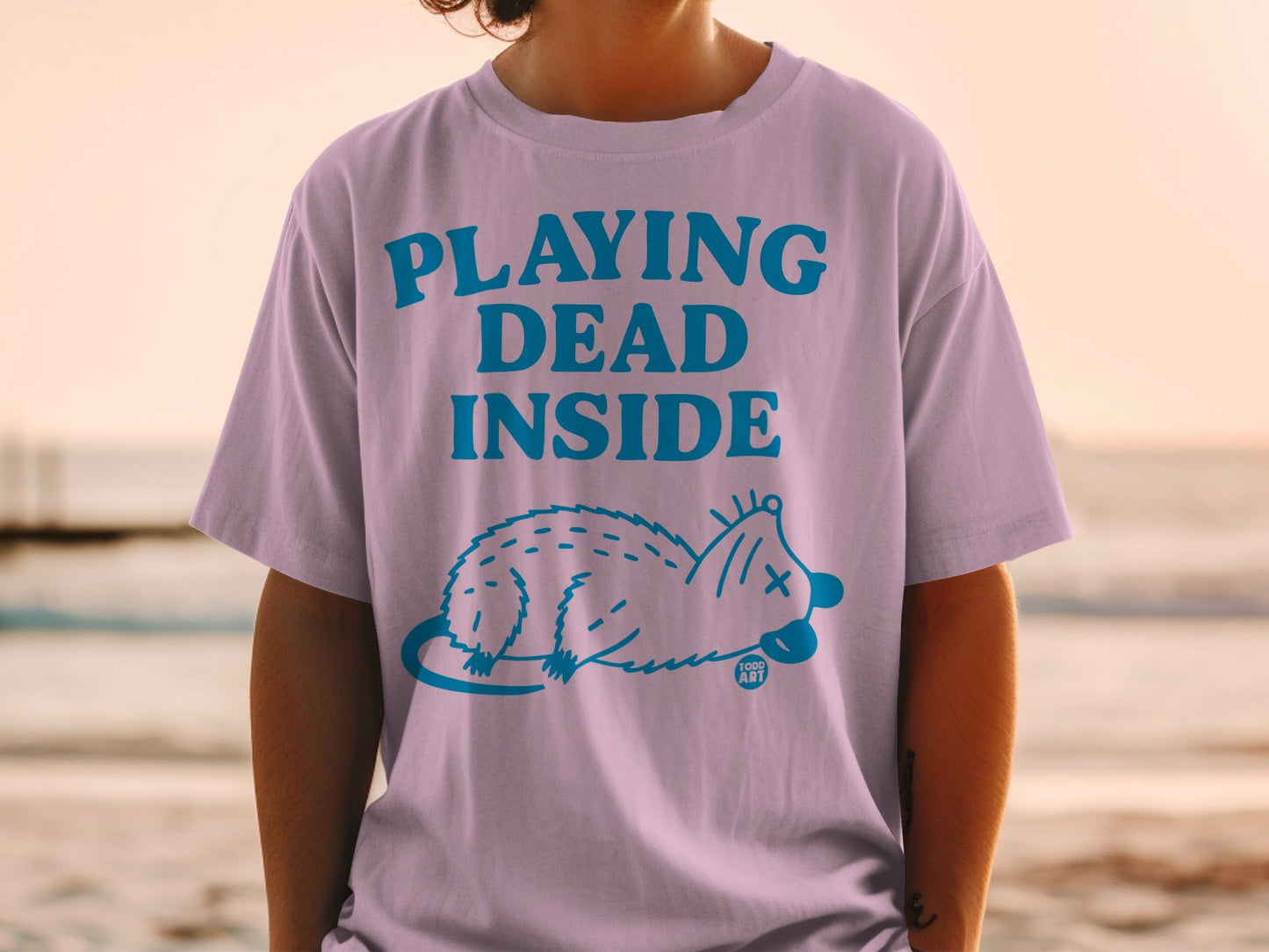 Pink t-shirt with "PLAYING DEAD INSIDE" text and a blue opossum graphic.