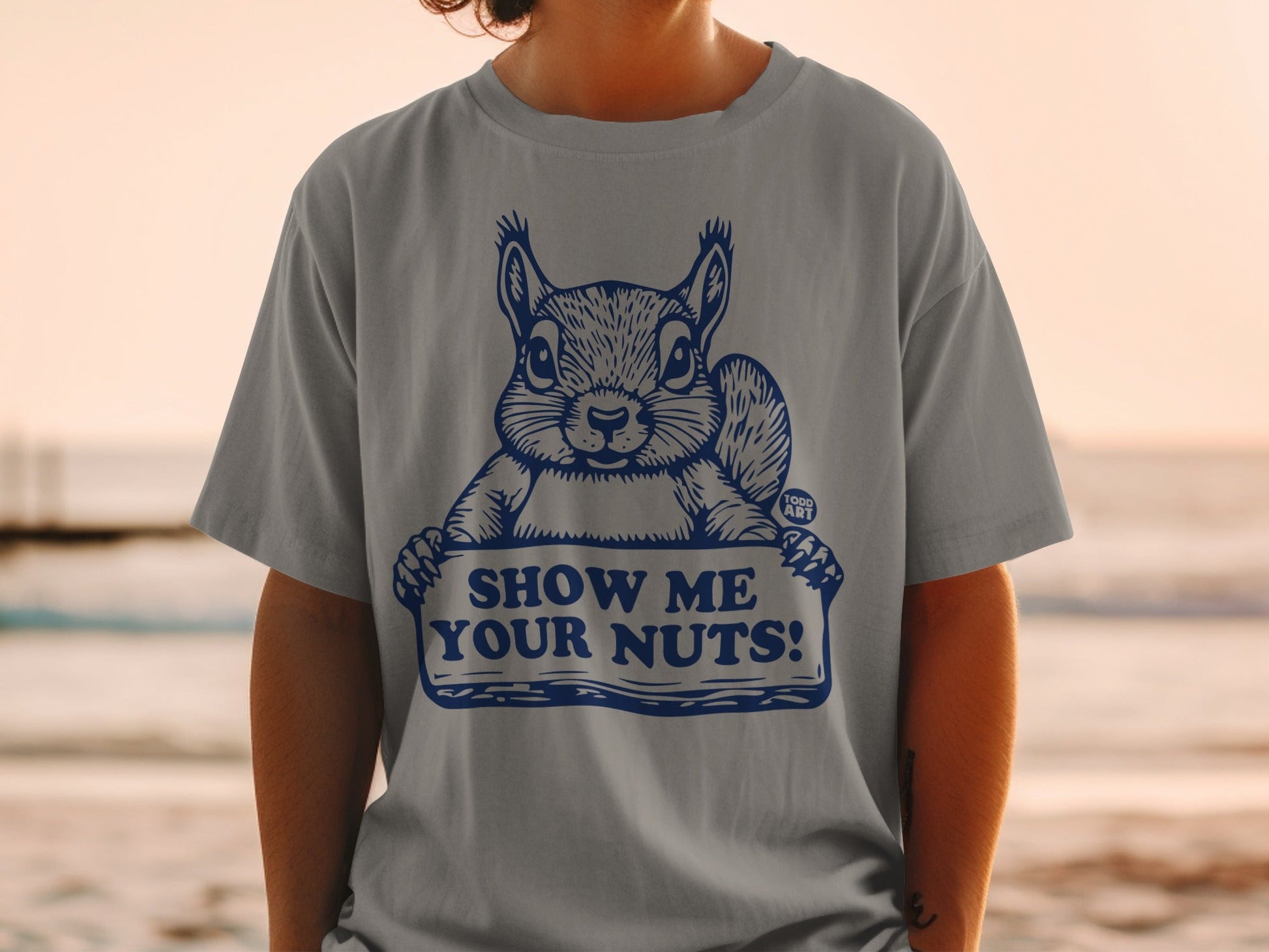 T-shirt with a squirrel holding a sign that says "SHOW ME YOUR NUTS!".