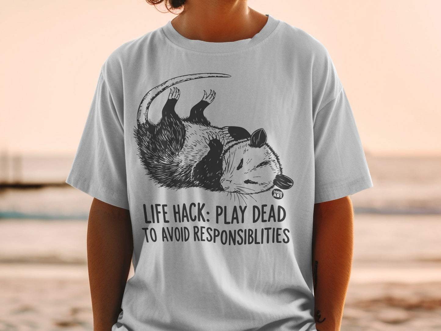 T-shirt with opossum graphic and text "LIFE HACK: PLAY DEAD TO AVOID RESPONSIBILITIES".