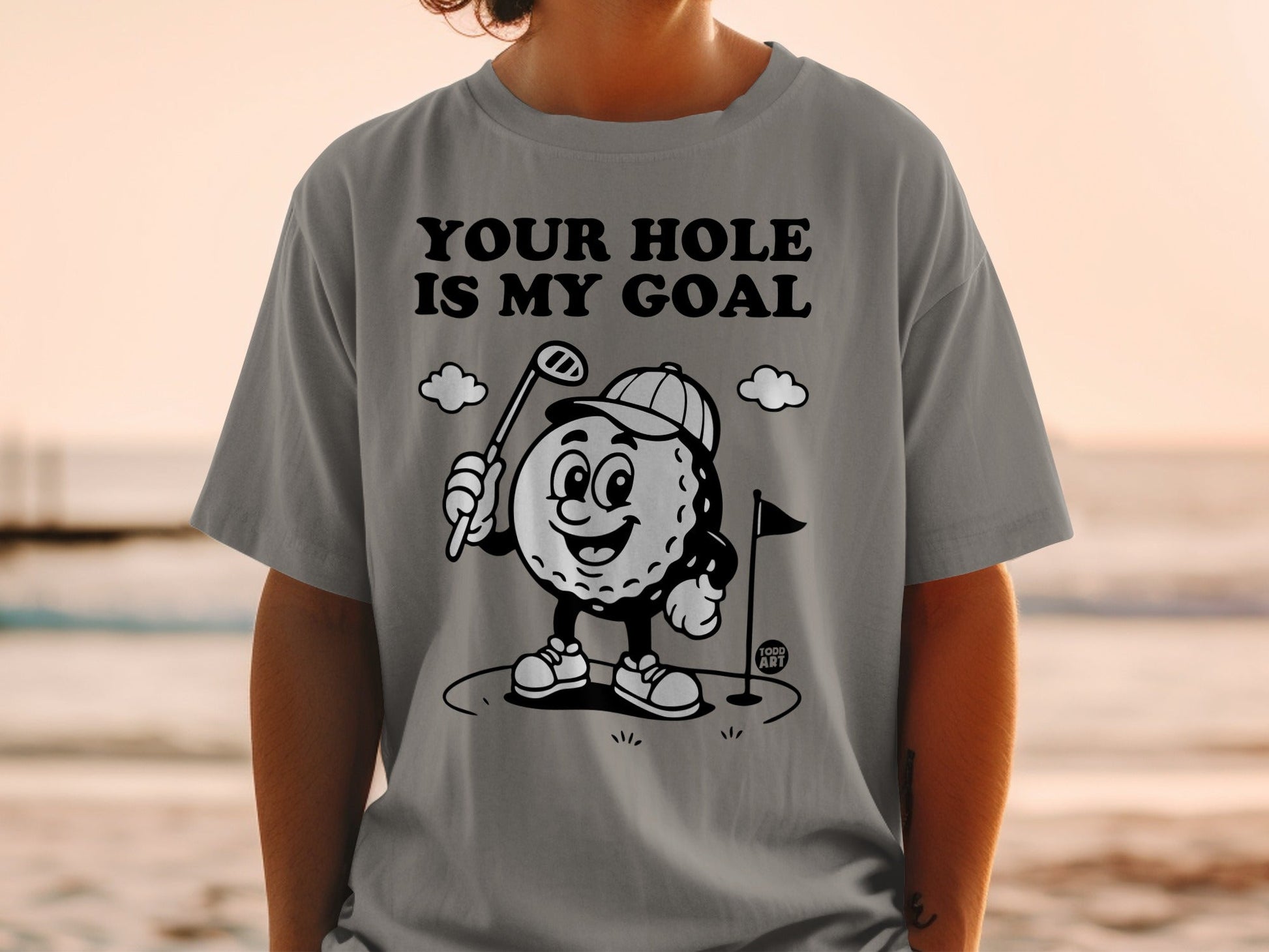 T-shirt with cartoon golf ball holding a club, text "YOUR HOLE IS MY GOAL".