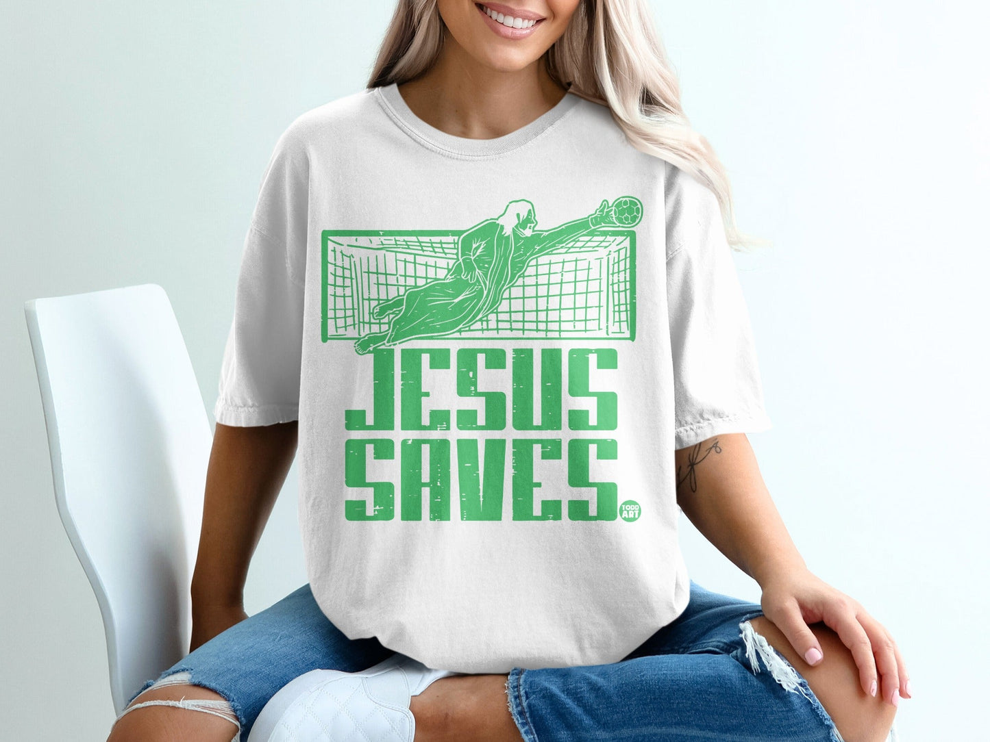 Green graphic on white t-shirt shows a soccer goalie with text "JESUS SAVES".