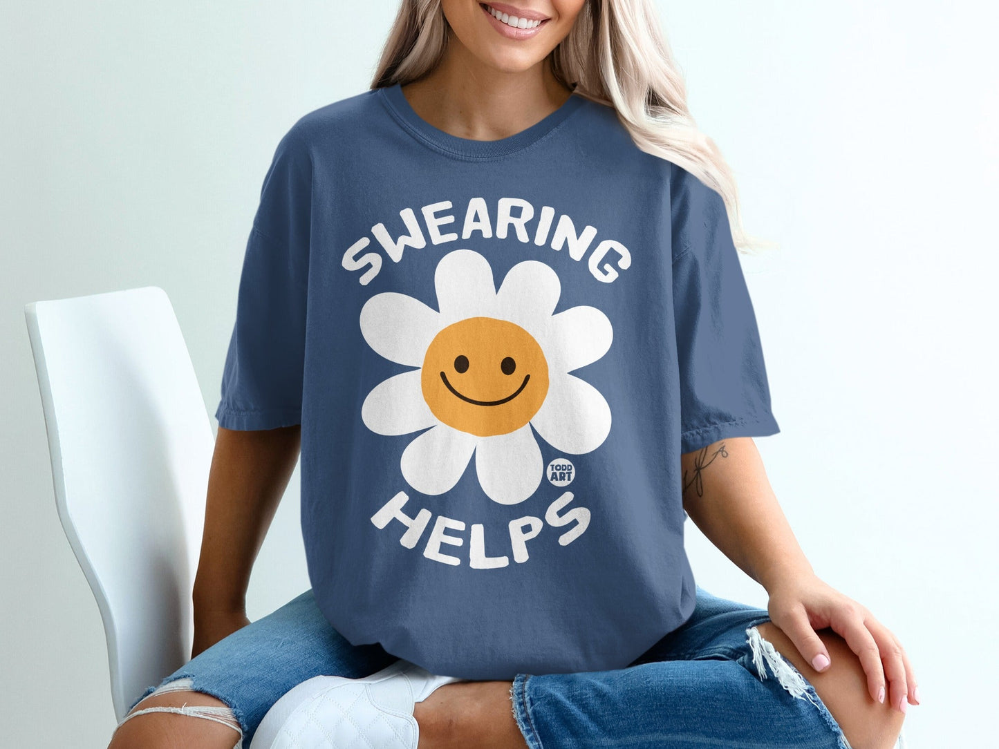 Blue t-shirt with smiling daisy graphic and text "SWEARING HELPS".