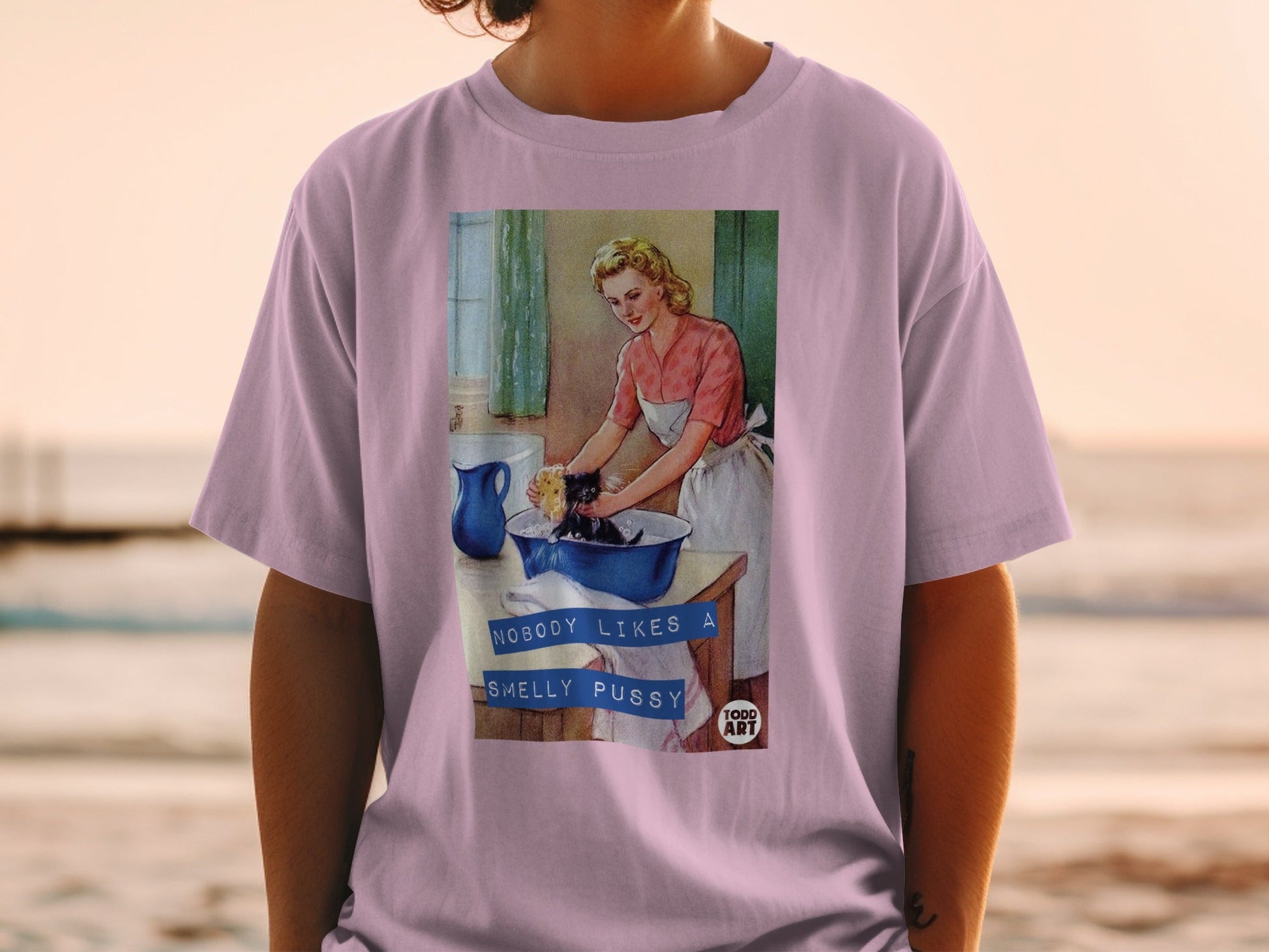 Pink t-shirt with graphic: Woman bathing cat, text "Nobody Likes A Smelly Pussy" and "TODD ART".