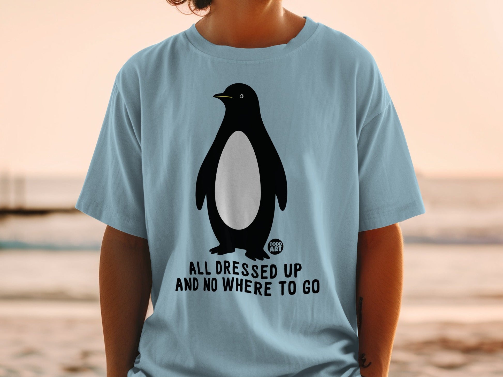 Light blue t-shirt with a penguin graphic and text that reads "ALL DRESSED UP AND NO WHERE TO GO".