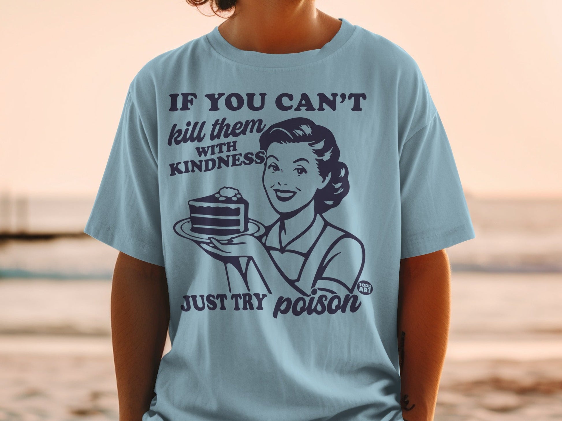 Light blue t-shirt with woman holding cake, text reads "kill them with kindness JUST TRY poison"
