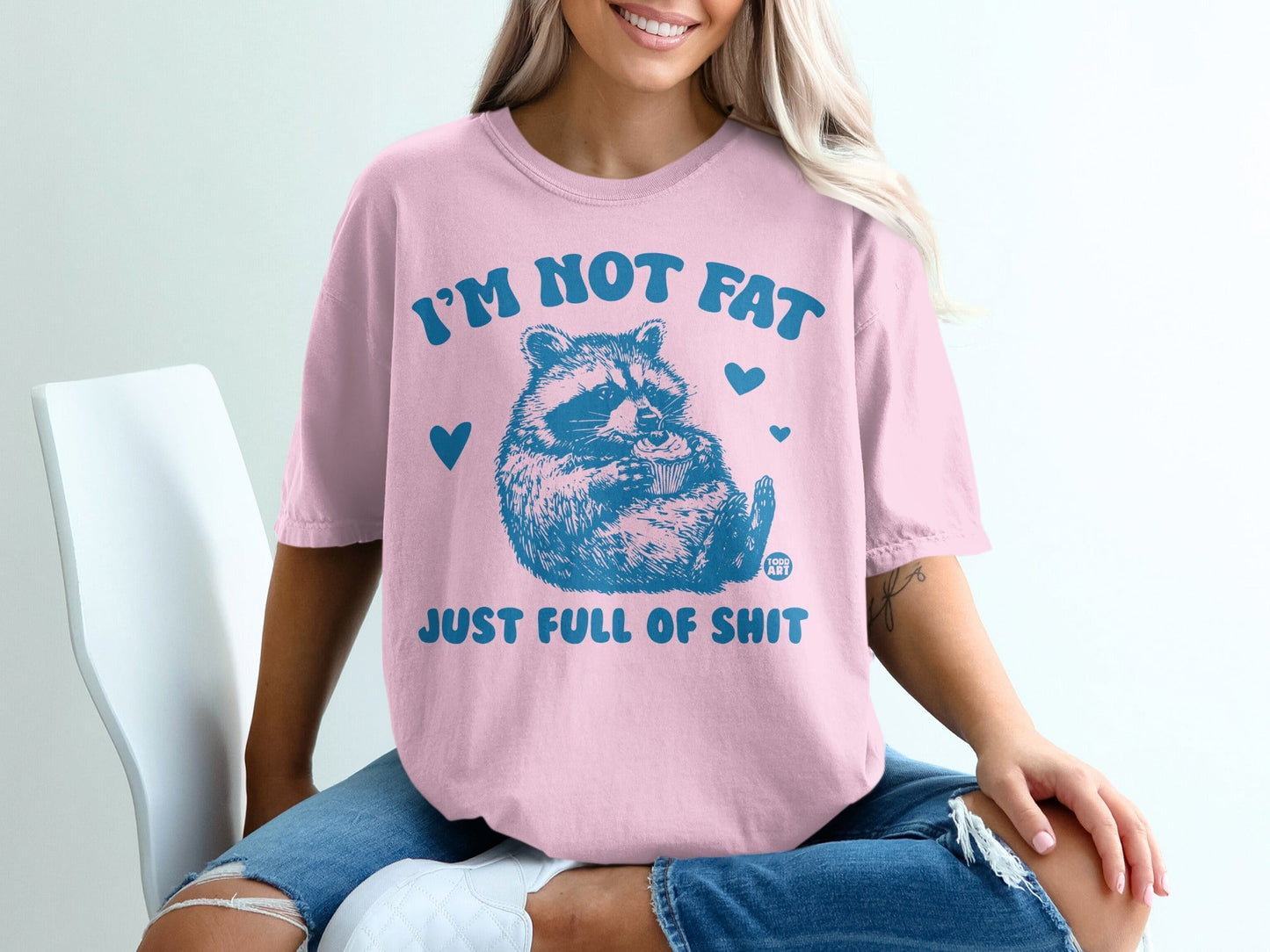 Pink t-shirt with raccoon holding cupcake and text "I'm not fat, just full of shit".